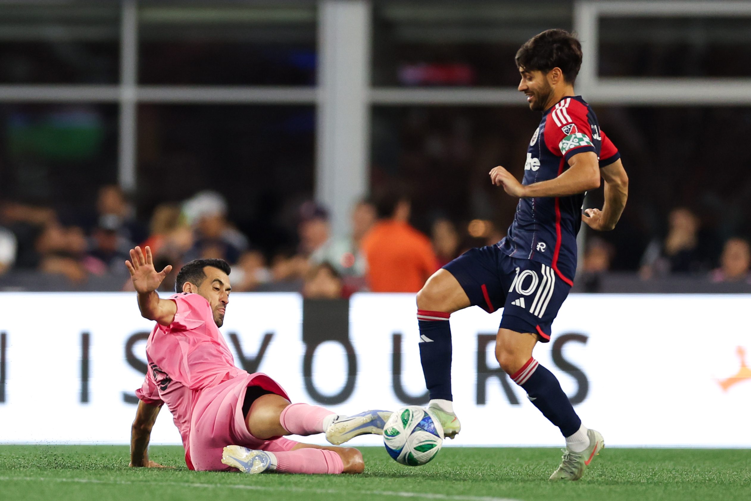 Jul 9, 2025; Foxborough, Massachusetts, USA; Inter Miami CF midfielder Sergio Busquets (5) slide tackles New England Revolution midfielder Carles Gil (10) during the first half at Gillette Stadium. Mandatory Credit: Paul Rutherford-Imagn Images