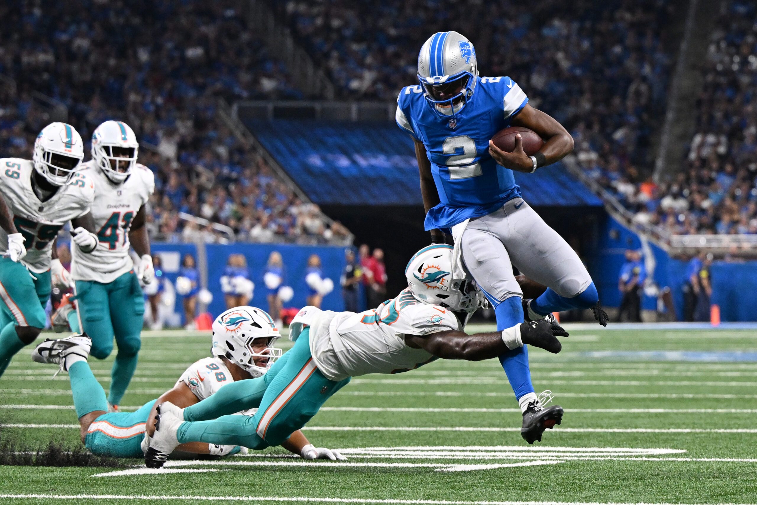 Aug 16, 2025; Detroit, Michigan, USA;  Detroit Lions quarterback Hendon Hooker (2) scrambles away from Miami Dolphins linebacker Dequan Jackson (57) to score a touchdown that was nullified by an offensive penalty in the third quarter at Ford Field. Mandatory Credit: Lon Horwedel-Imagn Images