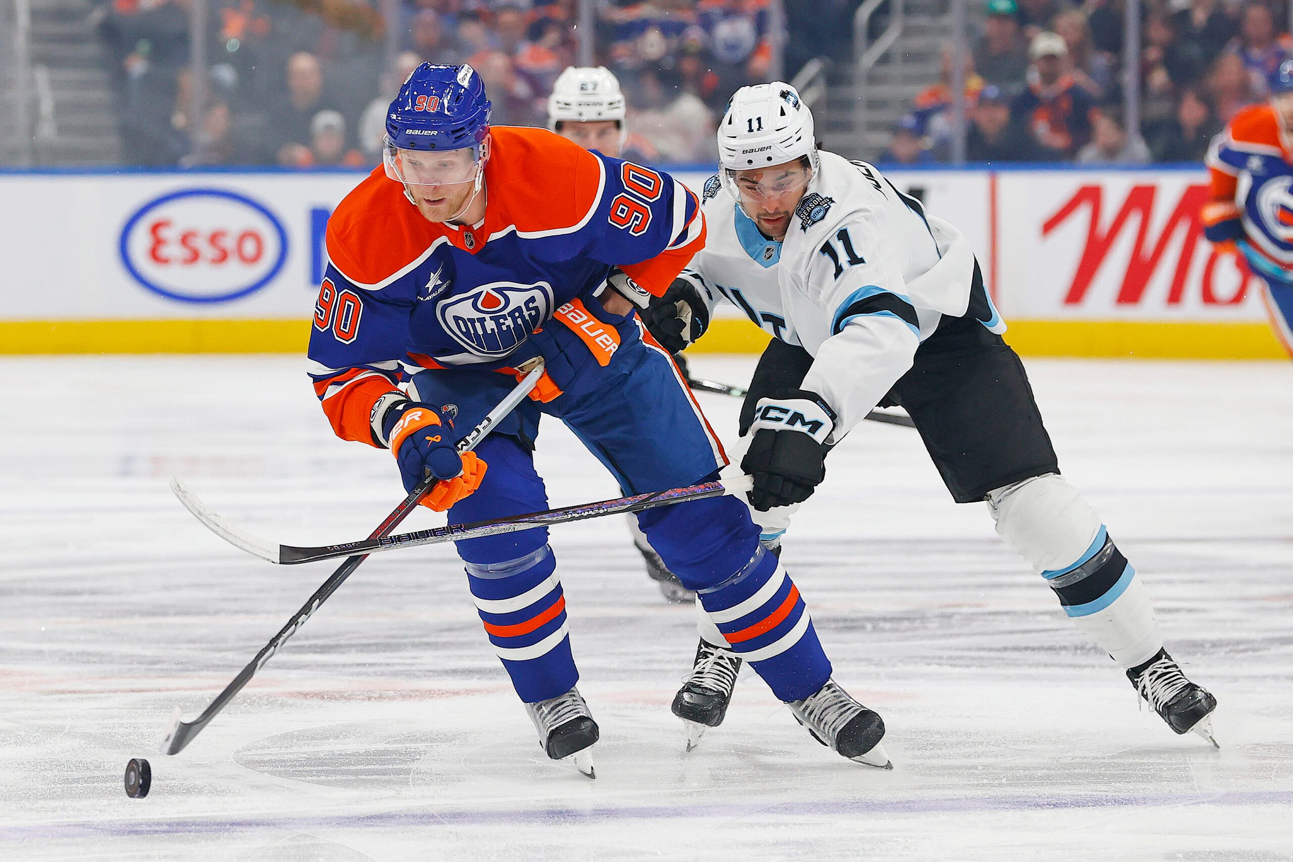 Mar 18, 2025; Edmonton, Alberta, CAN; Utah Hockey Club froward Dylan Guenther (11) tries to knock the puck away from Edmonton Oilers forward Corey Perry (90) during the first period at Rogers Place. Mandatory Credit: Perry Nelson-Imagn Images