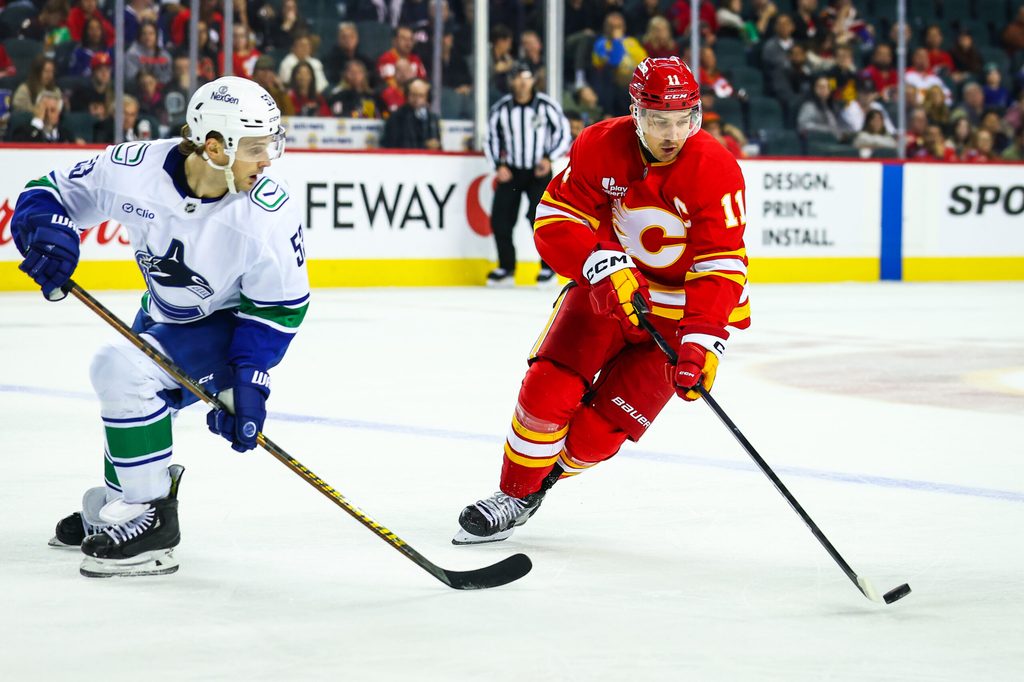 Oct 1, 2025; Calgary, Alberta, CAN; Calgary Flames center Mikael Backlund (11) controls the puck against Vancouver Canucks center Teddy Blueger (53) during the second period at Scotiabank Saddledome. Mandatory Credit: Sergei Belski-Imagn Images