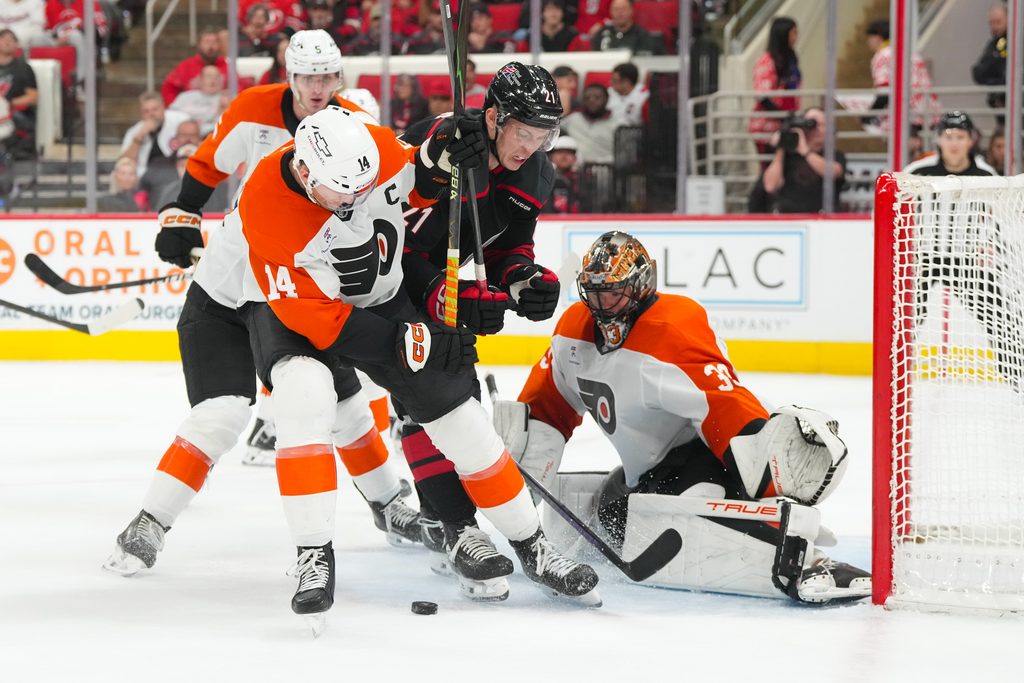 Oct 11, 2025; Raleigh, North Carolina, USA; Carolina Hurricanes defenseman Alexander Nikishin (21) and Philadelphia Flyers center Sean Couturier (14) battle over the loose puck in from of Philadelphia Flyers goaltender Samuel Ersson (33) during the third period at Lenovo Center. Mandatory Credit: James Guillory-Imagn Images