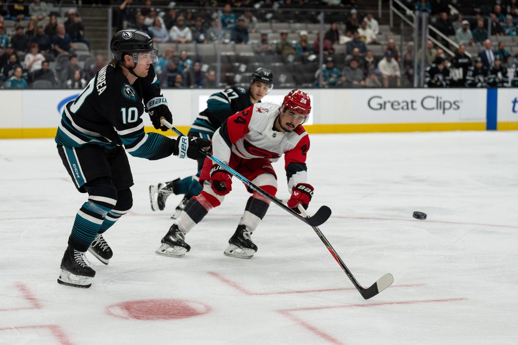 Oct 14, 2025; San Jose, California, USA; San Jose Sharks center Ty Dellandrea (10) shoots the puck past Carolina Hurricanes center Seth Jarvis (24) during the first period at SAP Center at San Jose. Mandatory Credit: Stan Szeto-Imagn Images