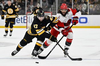 Nov 1, 2025; Boston, Massachusetts, USA; Boston Bruins center Mark Kastelic (47) and Carolina Hurricanes defenseman Jalen Chatfield (5) battle for control of the puck  during the third period at TD Garden. Mandatory Credit: Eric Canha-Imagn Images