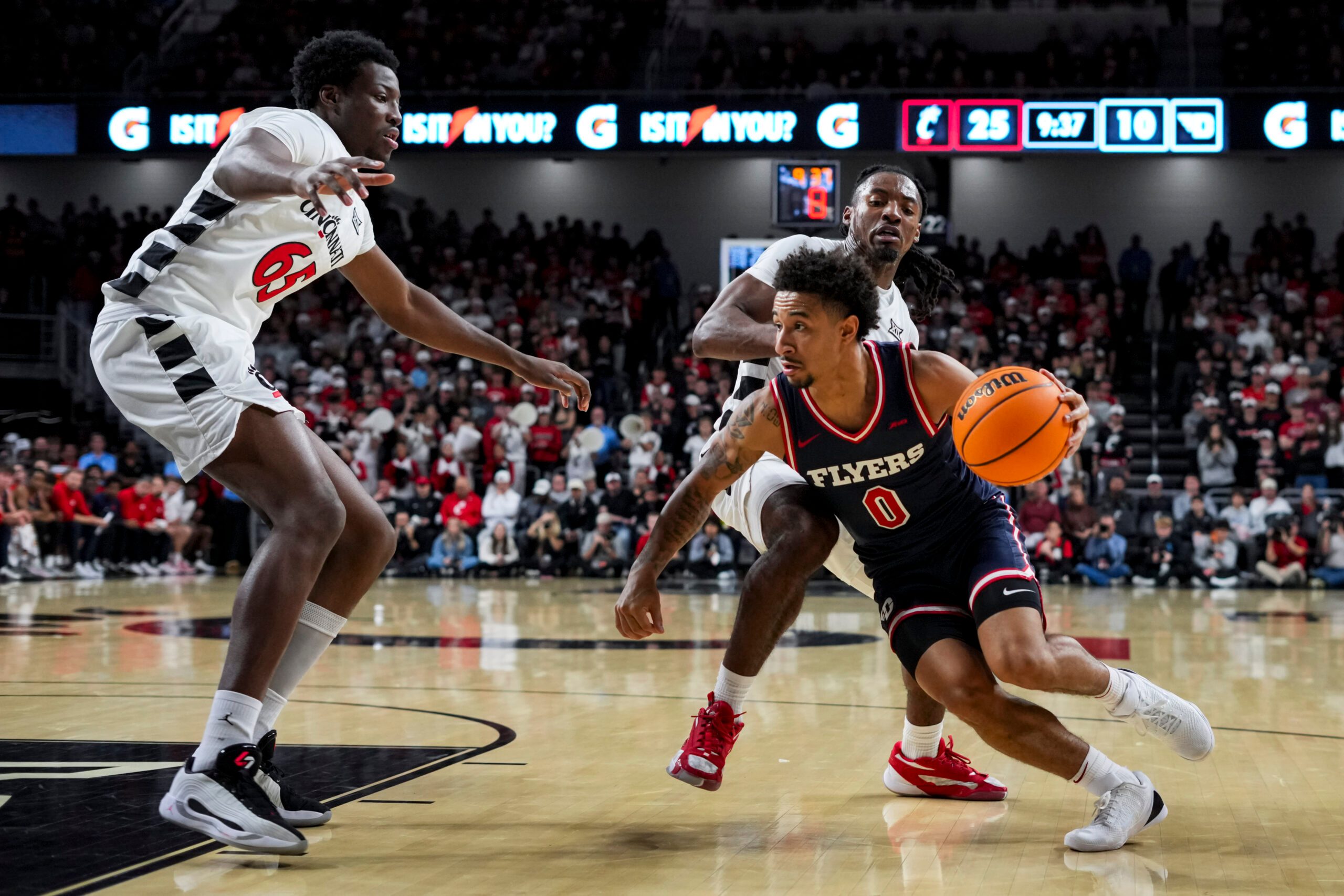 Nov 11, 2025; Cincinnati, Ohio, USA; Dayton Flyers guard Javon Bennett (0) drives to the basket against Cincinnati Bearcats guard Day Day Thomas (1) and forward Halvine Dzellat (65) in the first half at Fifth Third Arena. Mandatory Credit: Aaron Doster-Imagn Images