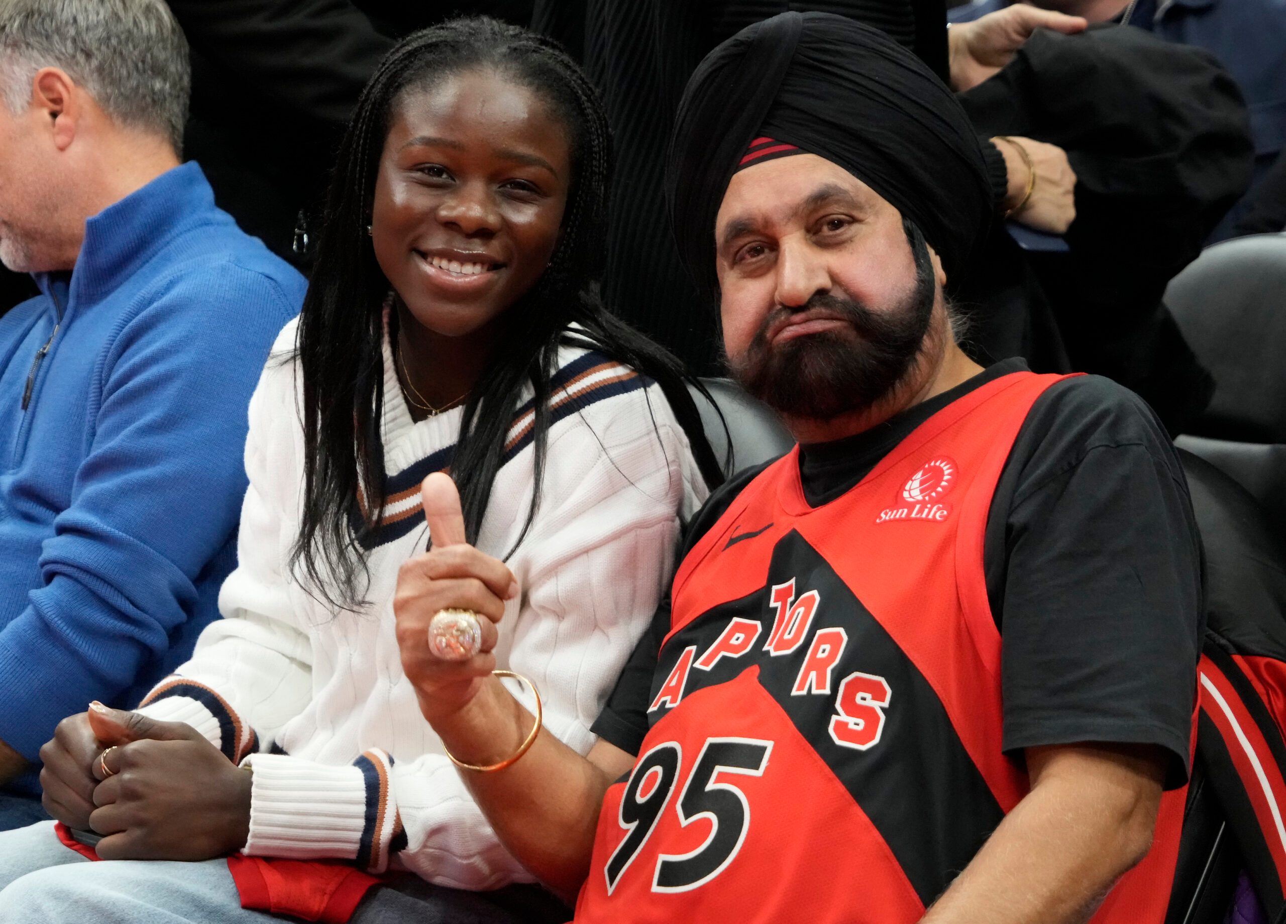 Nov 24, 2025; Toronto, Ontario, CAN; Canadian tennis star Victoria Mboko (left) sits court side with Toronto Raptors superfan Nav Bhatia (right) during a game between the Cleveland Cavaliers and Toronto Raptors during the second half at Scotiabank Arena. Mandatory Credit: John E. Sokolowski-Imagn Images