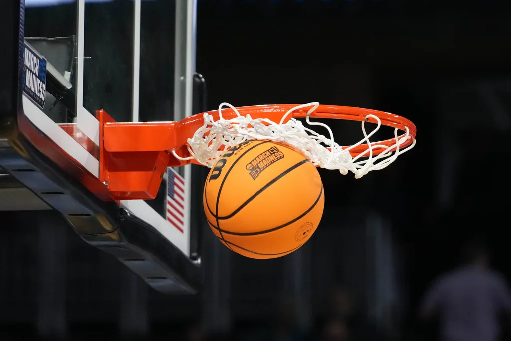 Mar 19, 2025; Wichita, KS, USA; A Wilson official NCAA Evo NXT basketball with the March Madness logo approaches the rim and the net at Intrust Bank Arena. Mandatory Credit: Kirby Lee-Imagn Images