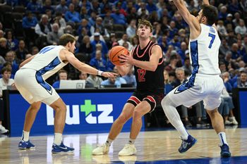 Nov 5, 2025; Omaha, Nebraska, USA;  South Dakota Coyotes guard Isaac Bruns (12) drives against Creighton Bluejays forward Isaac Traudt (41) and Fedor Zugic (7) during the first half at CHI Health Center Omaha. Mandatory Credit: Steven Branscombe-Imagn Images