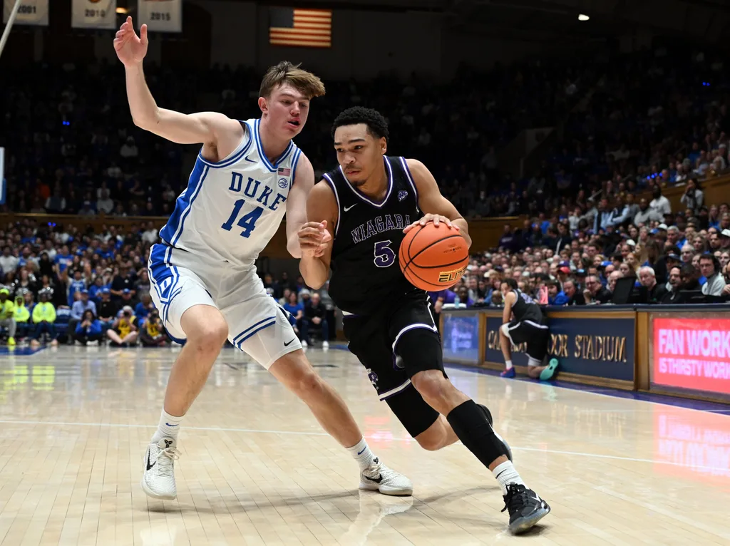Nov 21, 2025; Durham, North Carolina, USA;Niagara Purple Eagles guard Justin Page (5) drives to the basket as Duke Blue Devils forward Nikolas Khamenia (14) defends during the first half at Cameron Indoor Stadium. Mandatory Credit: Rob Kinnan-Imagn Images