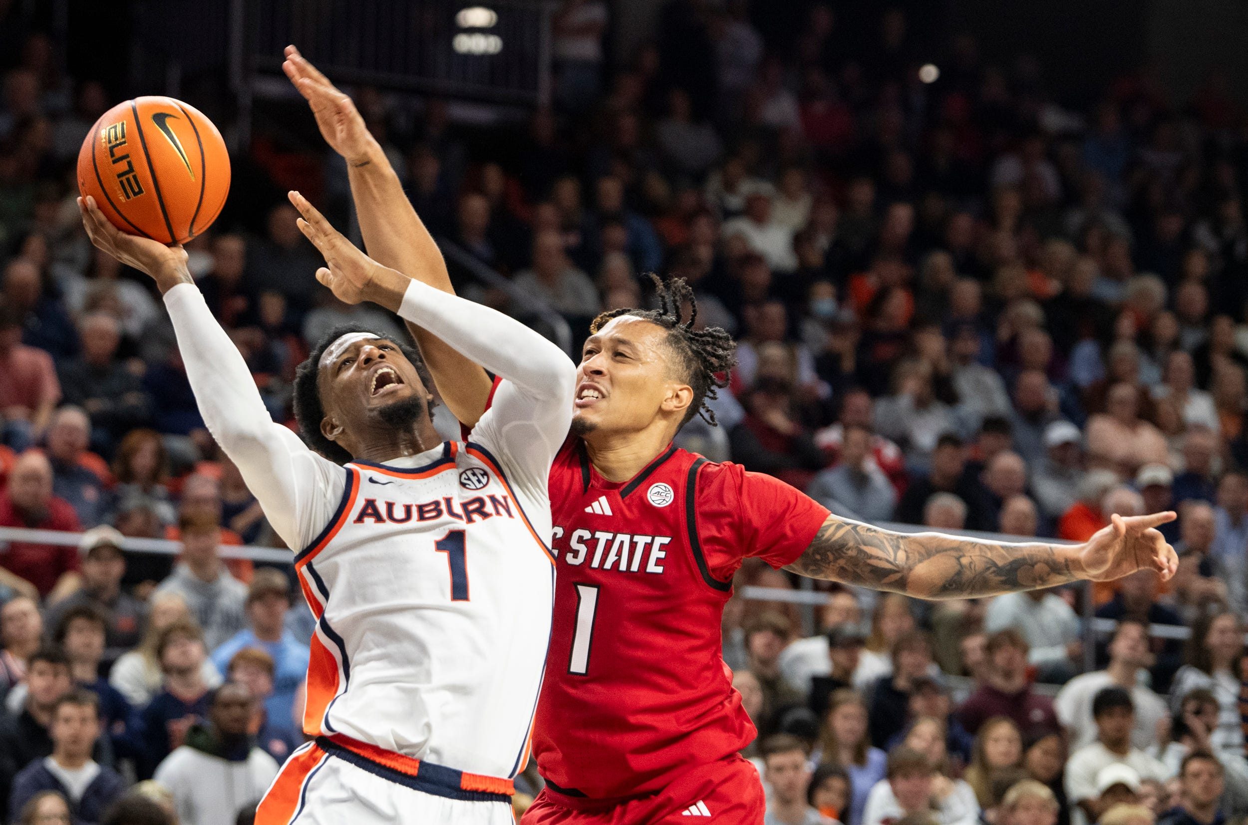 Auburn Tigers guard Kevin Overton (1) draws a foul from NC State Wolfpack forward Darrion Williams (1) as Auburn Tigers take on NC State Wolfpack at Neville Arena in Auburn, Ala. on Wednesday, Dec. 3, 2025. Auburn Tigers defeated NC State Wolfpack 83-73.
