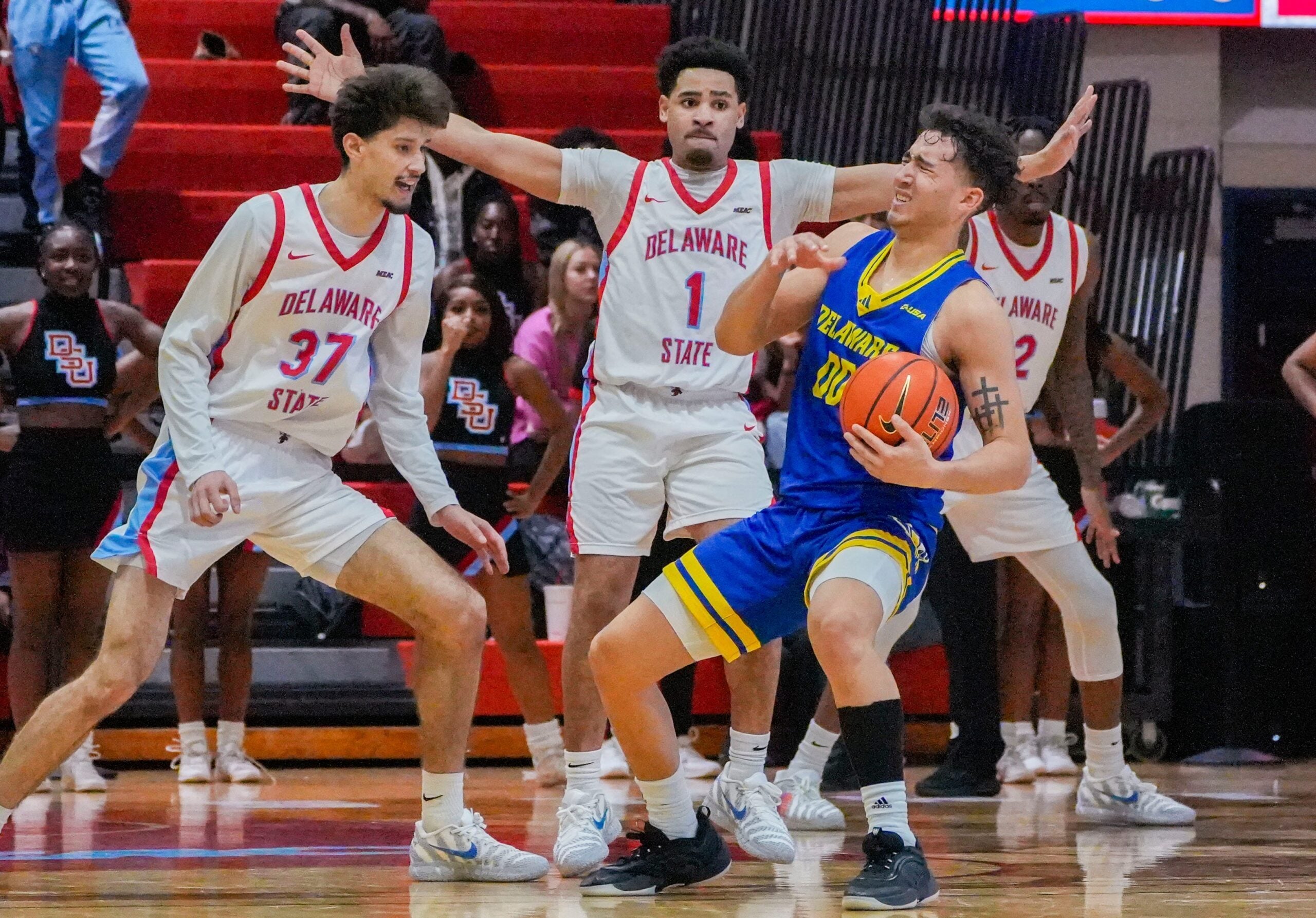 Delaware’s Christian Bliss (right) reacts after contact with Ponce James (1) and Ademar Santos in overtime in the Hornets’ 75-72 win at Delaware State’s Memorial Hall, Dec. 6, 2025.