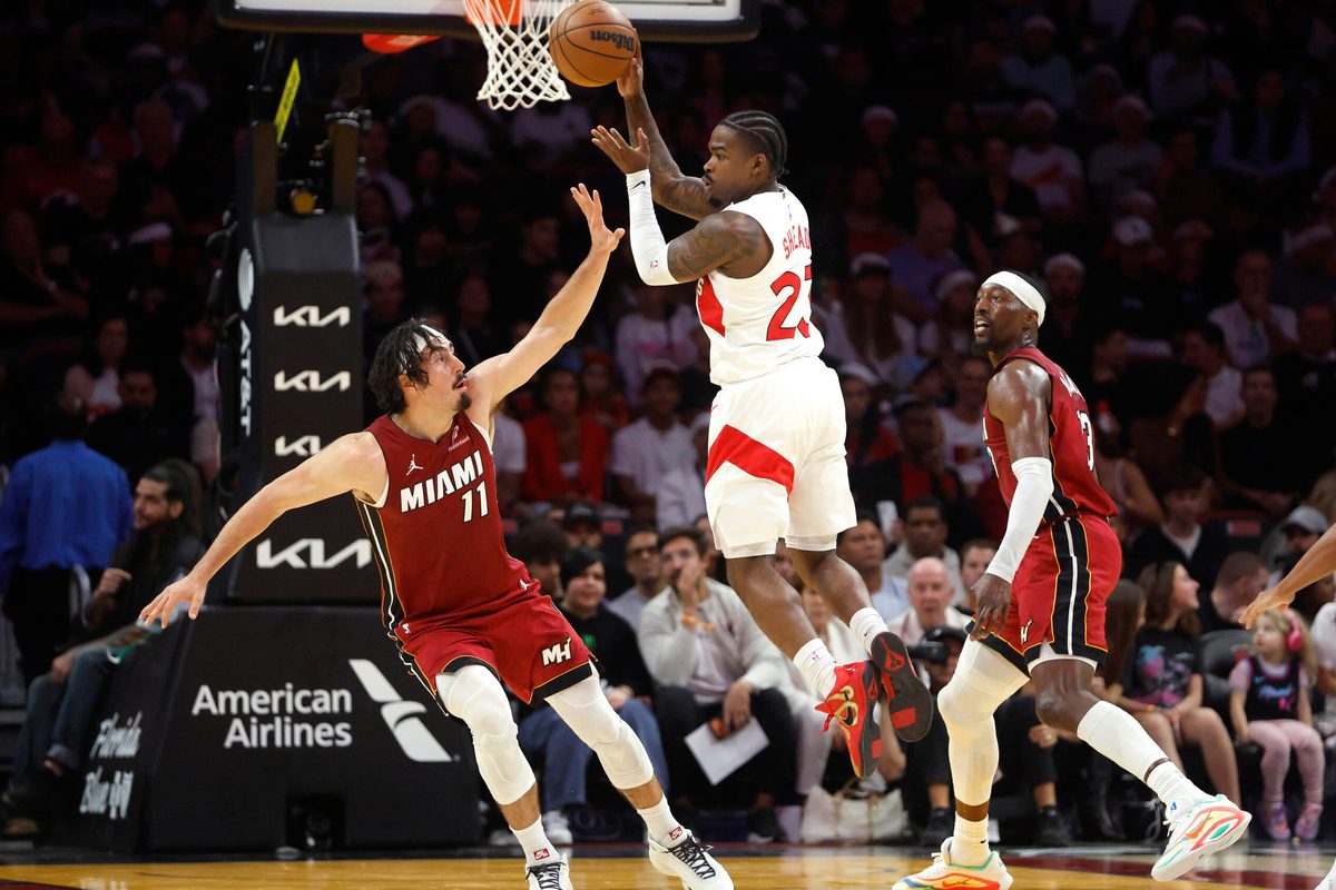 Dec 23, 2025; Miami, Florida, USA; Toronto Raptors guard Jamal Shead (23) passes between Miami Heat forward Jaime Jaquez Jr. (11) and center Bam Adebayo (13) during the second half at Kaseya Center. Mandatory Credit: Rhona Wise-Imagn Images
