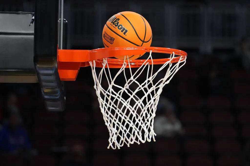 Mar 19, 2025; Wichita, KS, USA; A Wilson official NCAA Evo NXT basketball with the March Madness logo approaches the rim and the net at Intrust Bank Arena. Mandatory Credit: Kirby Lee-Imagn Images