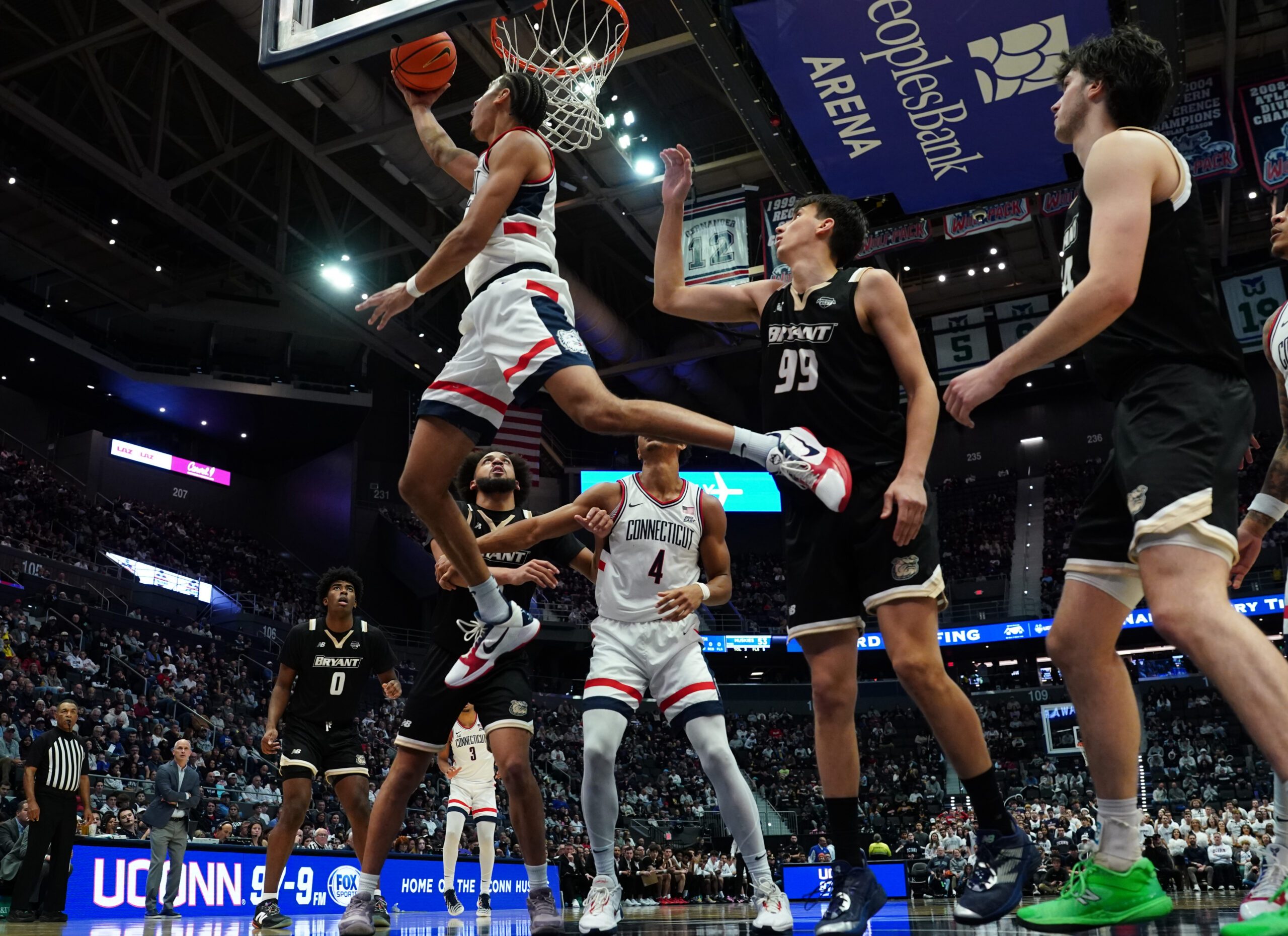 Nov 23, 2025; Hartford, Connecticut, USA; UConn Huskies forward Jayden Ross (23) makes the basket against Bryant Bulldogs guard Timofei Rudovskii (99) in the second half at Peoples Bank Arena. Mandatory Credit: David Butler II-Imagn Images