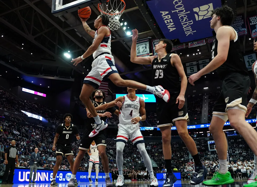 Nov 23, 2025; Hartford, Connecticut, USA; UConn Huskies forward Jayden Ross (23) makes the basket against Bryant Bulldogs guard Timofei Rudovskii (99) in the second half at Peoples Bank Arena. Mandatory Credit: David Butler II-Imagn Images