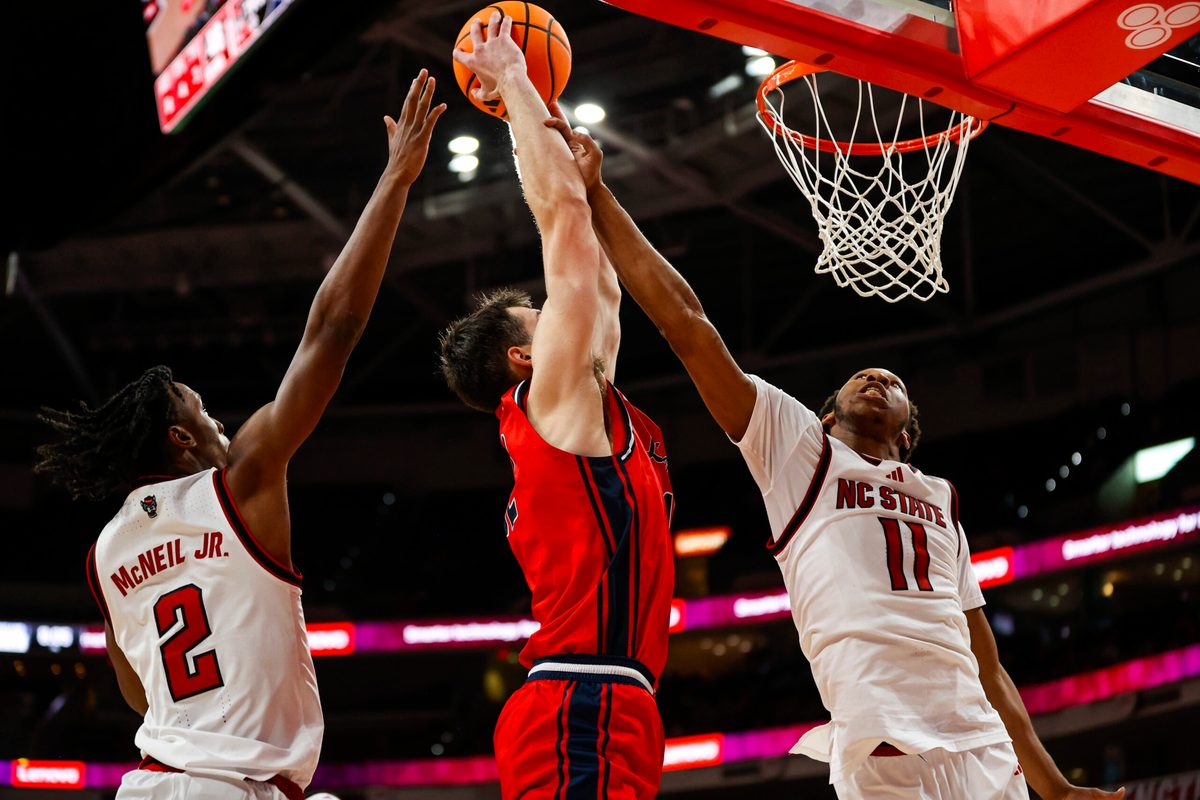 Dec 6, 2025; Raleigh, North Carolina, USA; Liberty Flames forward Josh Smith (12) attempts a dunk but is blocked by NC State Wolfpack guard Jr. Paul McNeil (2) and guard Quadir Copeland (11) during the second half of the game at Lenovo Center. Mandatory Credit: Jaylynn Nash-Imagn Images