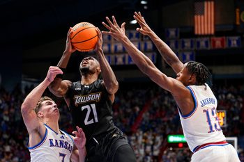 Dec 16, 2025; Lawrence, Kansas, USA; Towson Tigers guard Jack Doumbia Jr. (21) shoots against Kansas Jayhawks guard Kohl Rosario (7) and guard Elmarko Jackson (13) during the first half at Allen Fieldhouse. Mandatory Credit: Jay Biggerstaff-Imagn Images