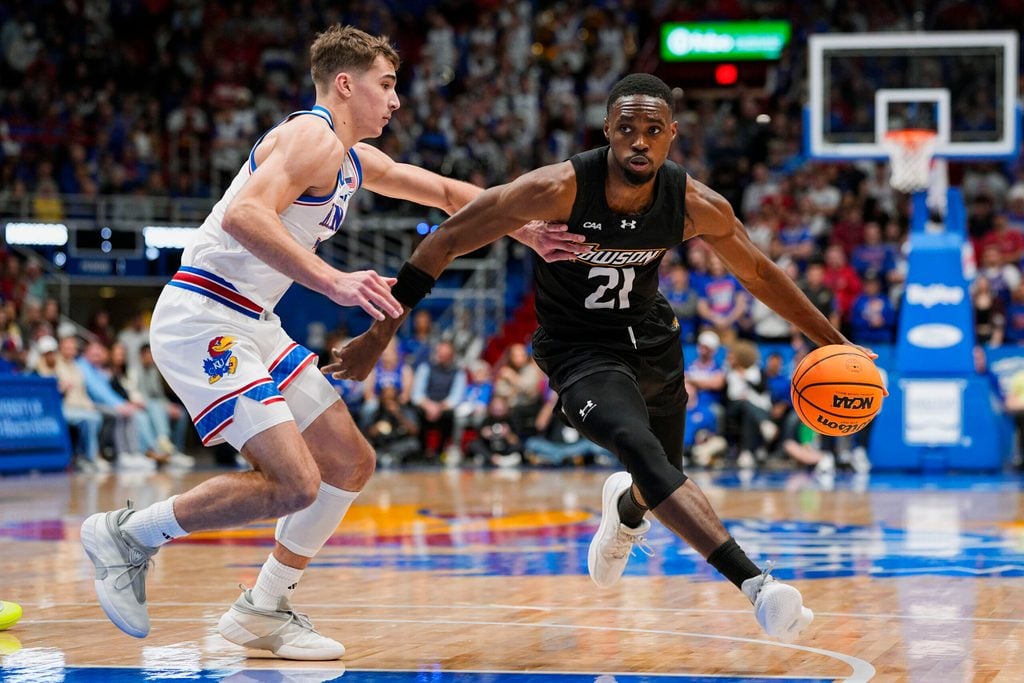 Dec 16, 2025; Lawrence, Kansas, USA; Towson Tigers guard Jack Doumbia Jr. (21) drives against Kansas Jayhawks guard Kohl Rosario (7) during the first half at Allen Fieldhouse. Mandatory Credit: Jay Biggerstaff-Imagn Images