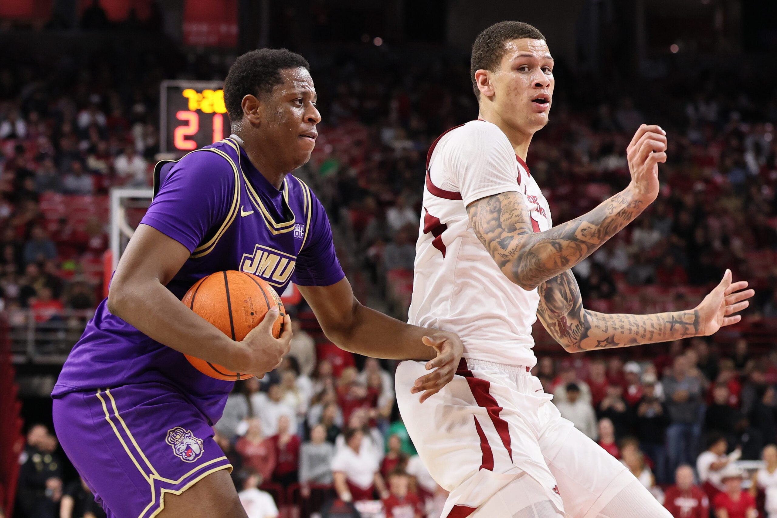 Dec 29, 2025; Fayetteville, Arkansas, USA; James Madison Dukes forward Justin McBride (21) drives against Arkansas Razorbacks forward Trevon Brazile (7) during the second half at Bud Walton Arena. Arkansas won 103-74. Mandatory Credit: Nelson Chenault-Imagn Images