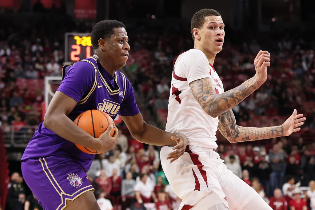 Dec 29, 2025; Fayetteville, Arkansas, USA; James Madison Dukes forward Justin McBride (21) drives against Arkansas Razorbacks forward Trevon Brazile (7) during the second half at Bud Walton Arena. Arkansas won 103-74. Mandatory Credit: Nelson Chenault-Imagn Images