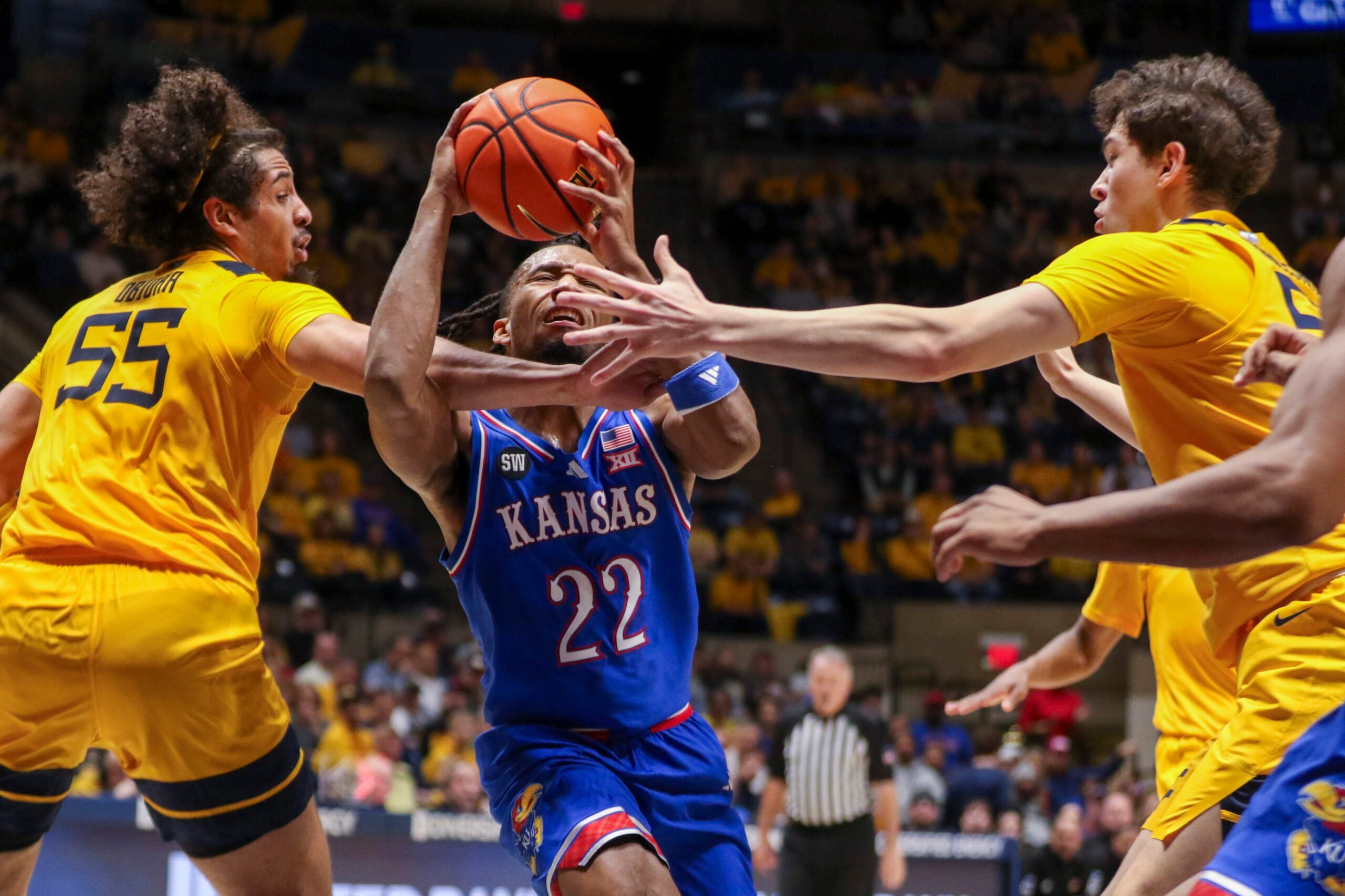 Jan 10, 2026; Morgantown, West Virginia, USA; Kansas Jayhawks guard Darryn Peterson (22) drives between West Virginia Mountaineers center Harlan Obioha (55) and West Virginia Mountaineers guard Treysen Eaglestaff (52) during the first half at Hope Coliseum. Mandatory Credit: Ben Queen-Imagn Images