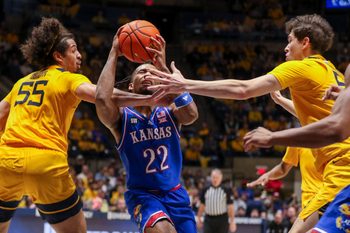 Jan 10, 2026; Morgantown, West Virginia, USA; Kansas Jayhawks guard Darryn Peterson (22) drives between West Virginia Mountaineers center Harlan Obioha (55) and West Virginia Mountaineers guard Treysen Eaglestaff (52) during the first half at Hope Coliseum. Mandatory Credit: Ben Queen-Imagn Images
