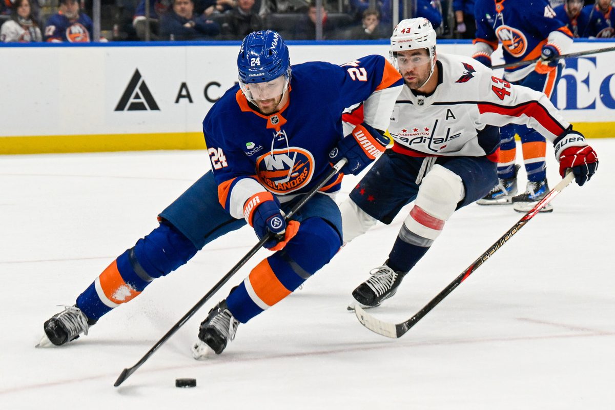 Nov 30, 2025; Elmont, New York, USA; New York Islanders defenseman Scott Mayfield (24) skate with the puck chased by Washington Capitals right wing Tom Wilson (43) during the first period at UBS Arena. Mandatory Credit: Dennis Schneidler-Imagn Images