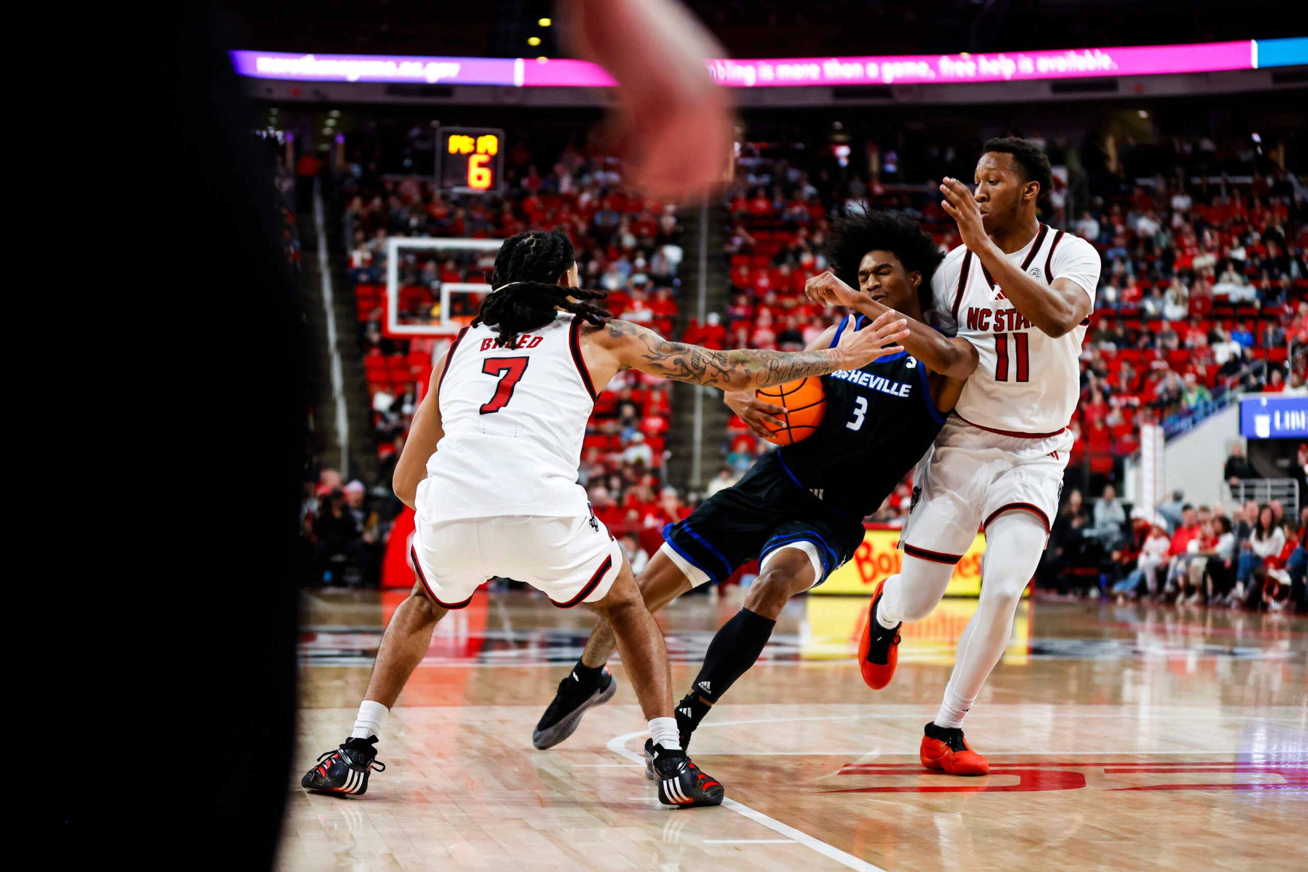 Dec 6, 2025; Raleigh, North Carolina, USA; UNC Asheville Bulldogs guard Kameron Taylor (3) is fouled on by NC State Wolfpack guard Alyn Breed (7) and guard Quadir Copeland (11) during the second half of the game at Lenovo Center. Mandatory Credit: Jaylynn Nash-Imagn Images