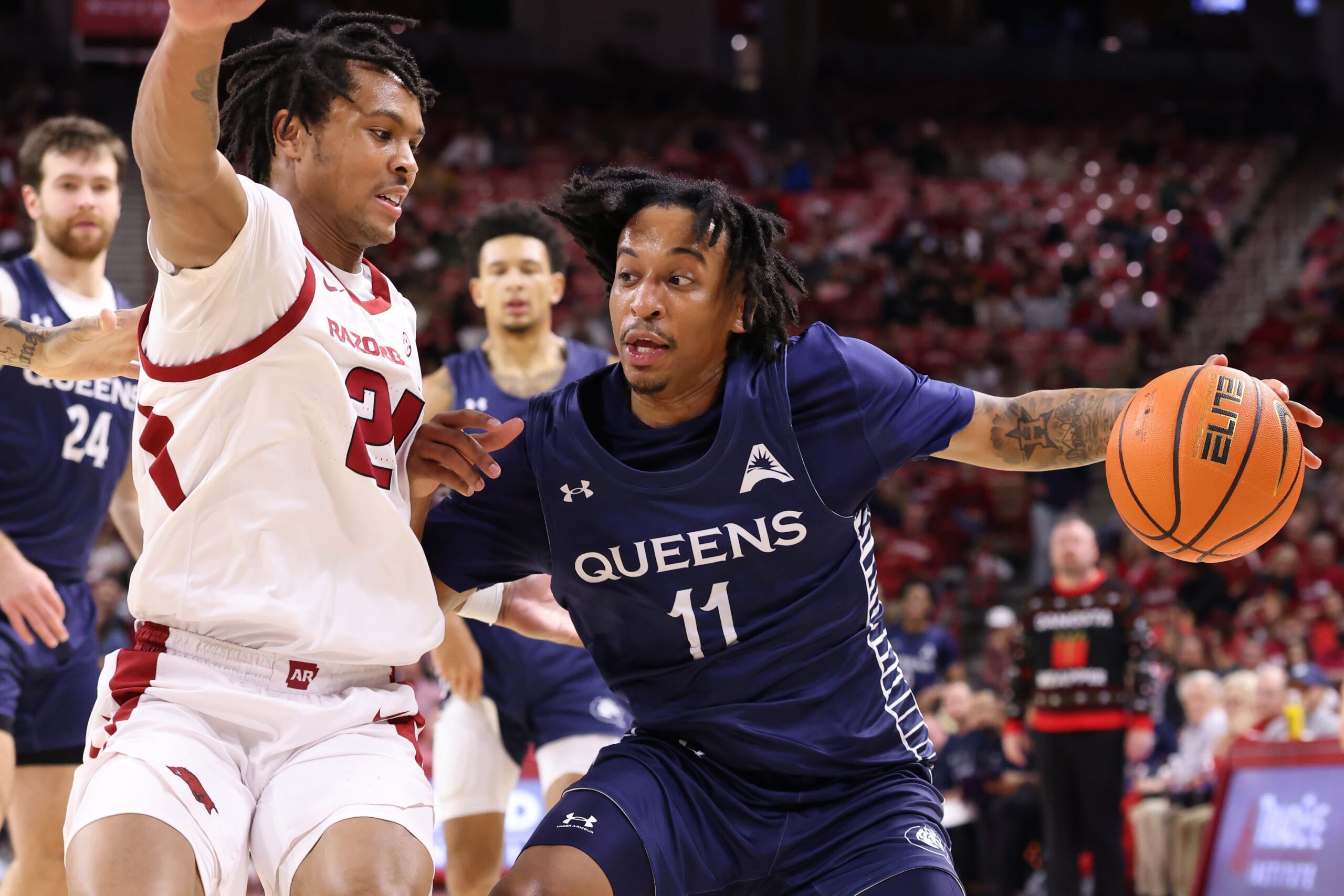Dec 16, 2025; Fayetteville, Arkansas, USA; Queens Royals guard Chris Ashby (11) drives against Arkansas Razorbacks guard D.J. Wagner (21) during the first half at Bud Walton Arena. Mandatory Credit: Nelson Chenault-Imagn Images