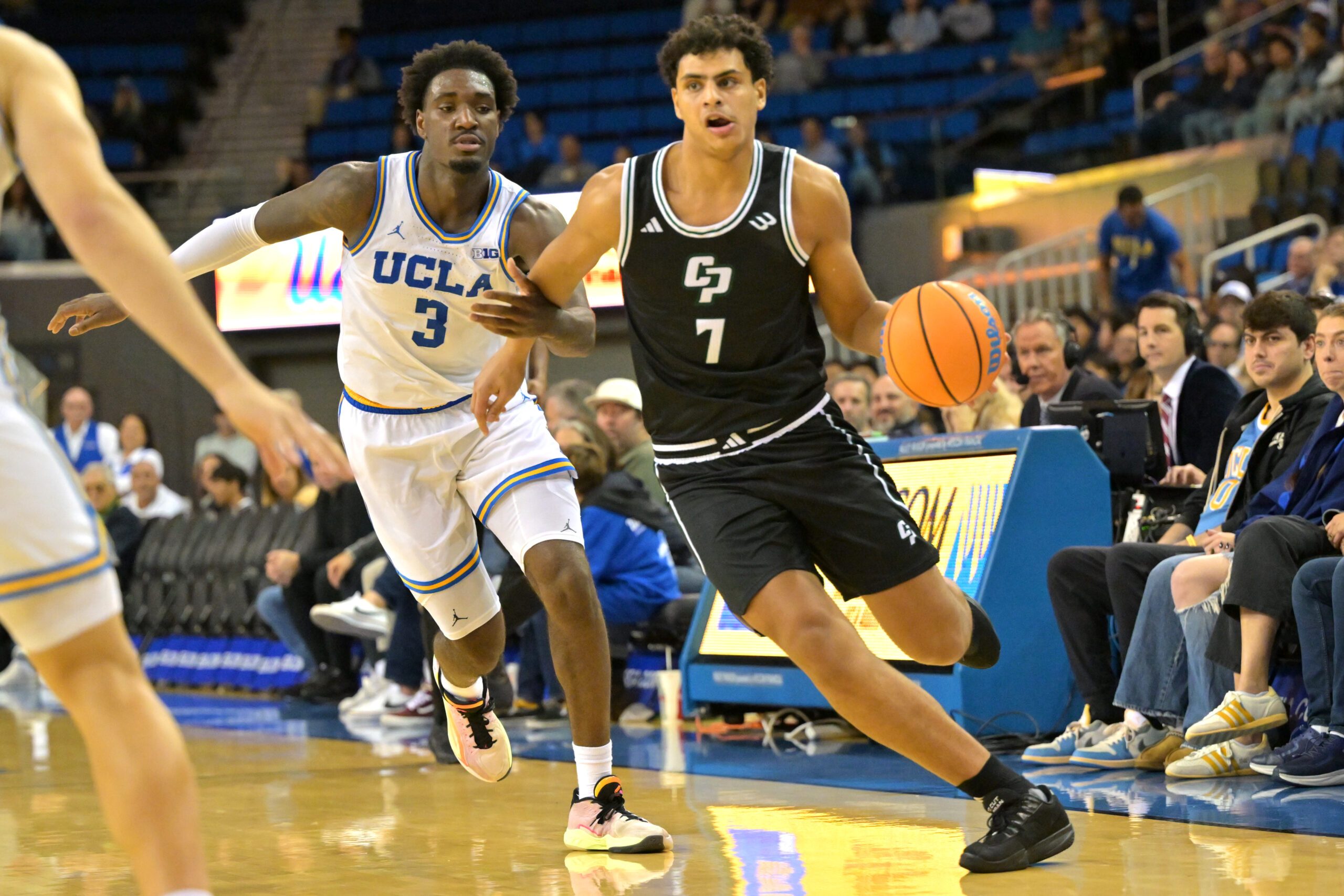 Dec 19, 2025; Los Angeles, California, USA;Cal Poly Mustangs forward Ali Assran (7) drives past UCLA Bruins guard Eric Dailey Jr. (3) during the second half at Pauley Pavilion presented by Wescom Financial. Mandatory Credit: Jayne Kamin-Oncea-Imagn Images