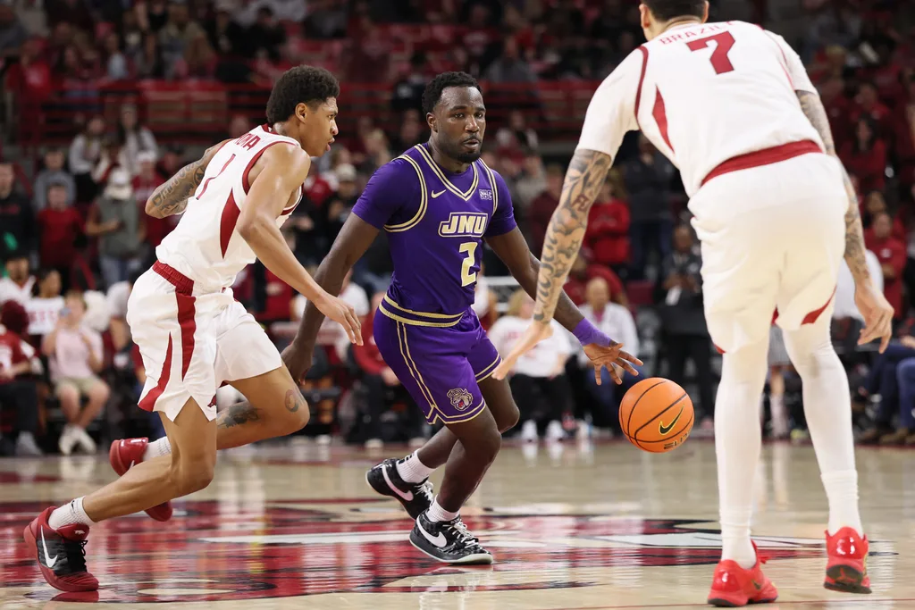 Dec 29, 2025; Fayetteville, Arkansas, USA; James Madison Dukes guard Bradley Douglas (2) drives against Arkansas Razorbacks guard Meleek Thomas (1) during the second half at Bud Walton Arena. Arkansas won 103-74. Mandatory Credit: Nelson Chenault-Imagn Images