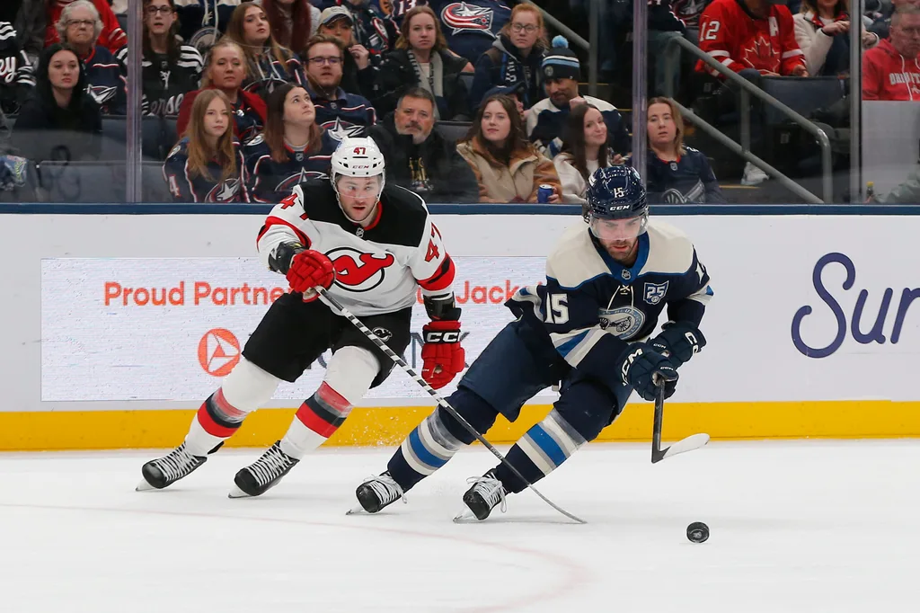 Dec 31, 2025; Columbus, Ohio, USA; Columbus Blue Jackets defenseman Dante Fabbro (15) carries the puck away from New Jersey Devils left wing Paul Cotter (47) during the third period at Nationwide Arena. Mandatory Credit: Russell LaBounty-Imagn Images