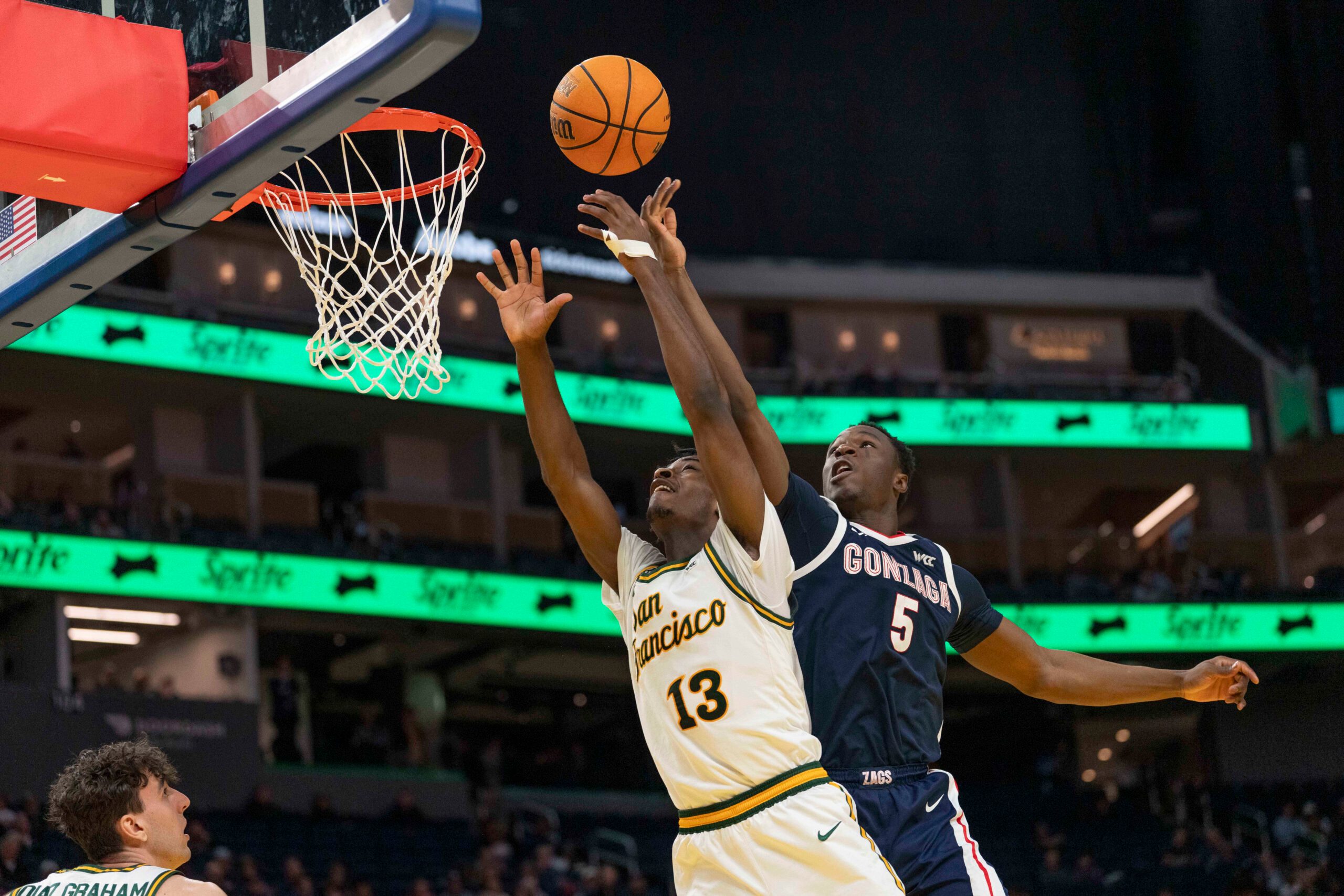 Feb 18, 2026; San Francisco, California, USA;  San Francisco Dons guard Legend Smiley (13) and Gonzaga Bulldogs forward Emmanuel Innocenti (5) reach for the ball during the second half at Chase Center. Mandatory Credit: Stan Szeto-Imagn Images