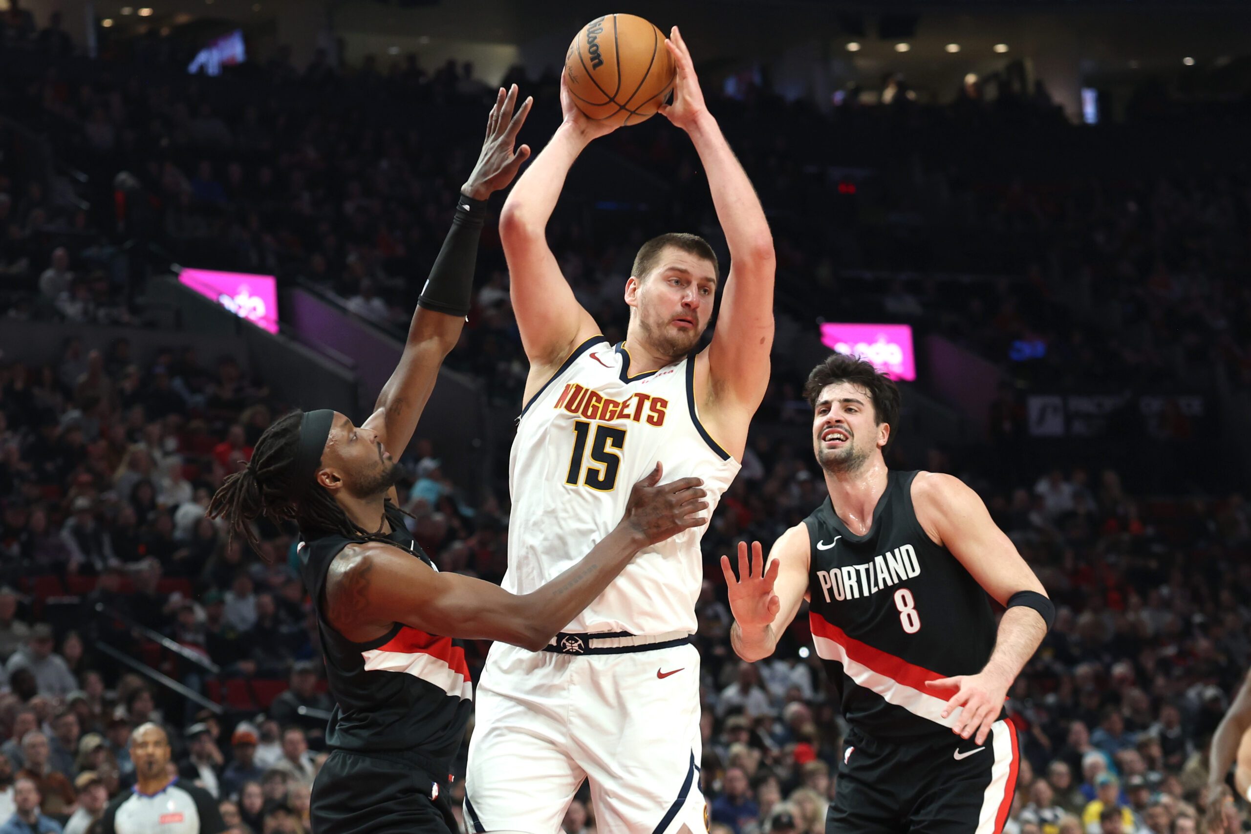 Feb 20, 2026; Portland, Oregon, USA; Denver Nuggets center Nikola Jokic (15) grabs a rebound over Portland Trail Blazers guard Jrue Holiday (5) and forward Deni Avdija (8) during first half at Moda Center. Mandatory Credit: Jaime Valdez-Imagn Images