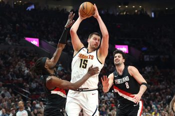 Feb 20, 2026; Portland, Oregon, USA;  Denver Nuggets center Nikola Jokic (15) grabs a rebound over Portland Trail Blazers guard Jrue Holiday (5) and forward Deni Avdija (8) during first half at Moda Center. Mandatory Credit: Jaime Valdez-Imagn Images