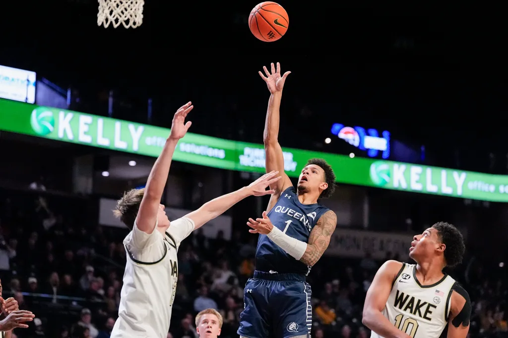 Dec 14, 2025; Winston-Salem, North Carolina, USA; Queens University Royals guard Nasir Mann (1) shoots the ball against Wake Forest Demon Deacons guard Isaac Carr (7) during the second half at Lawrence Joel Veterans Memorial Coliseum. Mandatory Credit: Jim Dedmon-Imagn Images