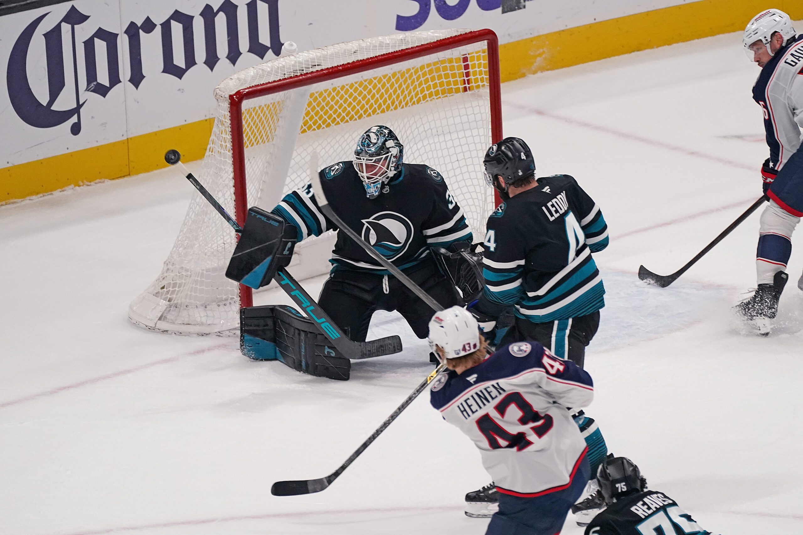 Jan 6, 2026; San Jose, California, USA; San Jose Sharks goaltender Alex Nedeljkovic (33) makes a save against Columbus Blue Jackets left winger Danton Heinen (43) as San Jose Sharks defenseman Nick Leddy (4) helps defend in the third period at SAP Center at San Jose. Mandatory Credit: David Gonzales-Imagn Images