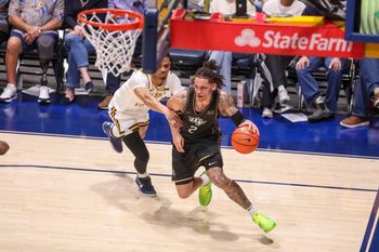 Mar 6, 2026; Morgantown, West Virginia, USA; UCF Knights guard Riley Kugel (2) dribbles along the baseline past West Virginia Mountaineers guard Jasper Floyd (1) during the first half at Hope Coliseum. Mandatory Credit: Ben Queen-Imagn Images