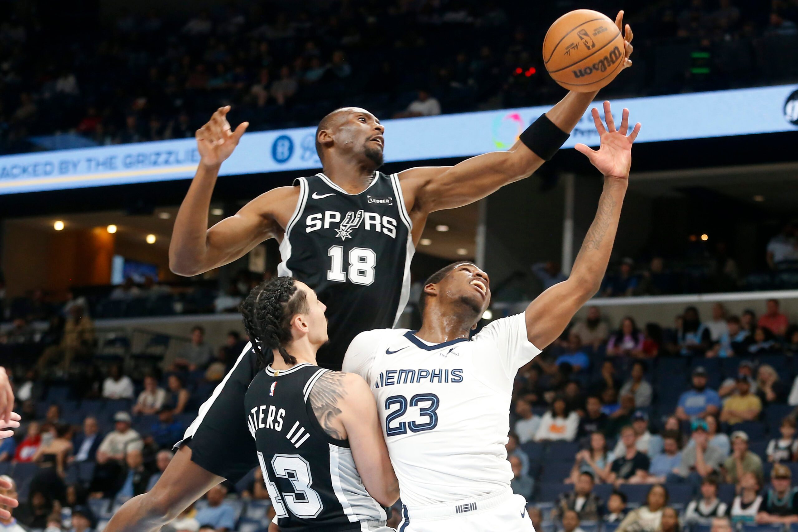 Mar 25, 2026; Memphis, Tennessee, USA; San Antonio Spurs center Bismack Biyombo (18) collects a rebound over forward Lindy Waters III (43) and Memphis Grizzlies forward Cedric Coward (23) during the fourth quarter at FedExForum. Mandatory Credit: Petre Thomas-Imagn Images
