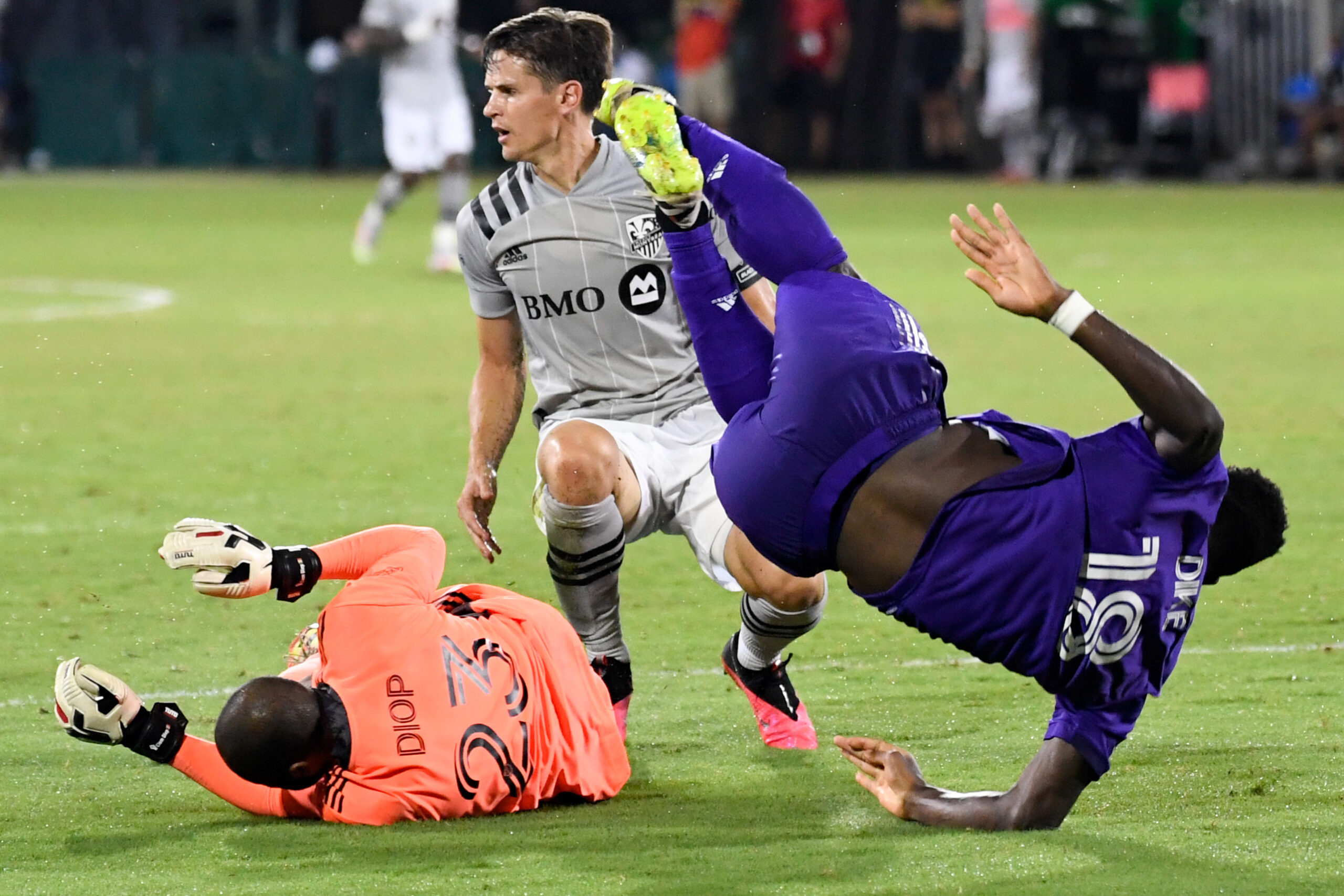 Jul 25, 2020; Orlando, Florida, USA; Orlando City SC forward Daryl Dike (18) dribbles the ball as Montreal Impact defender Jukka Raitala (22) tackles and goalkeeper Clement Diol (23) defends during the second half at ESPN Wide World of Sports Complex. Mandatory Credit: Douglas DeFelice-Imagn Images