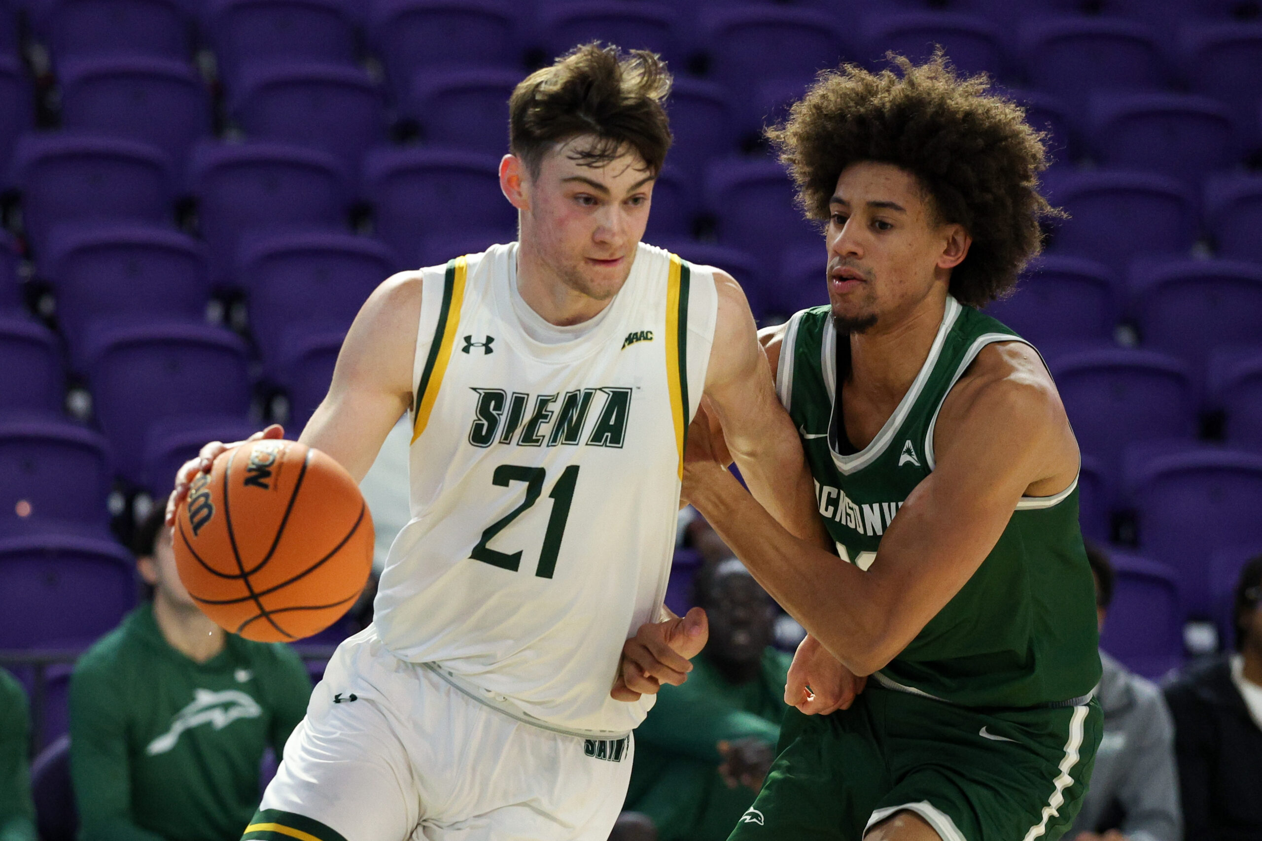 Nov 26, 2024; Fort Myers, Florida, USA; Siena Saints forward Brendan Coyle (21) drives to the basket past Jacksonville Dolphins forward Zimi Nwokeji (16) in the first half at Suncoast Credit Union Arena. Mandatory Credit: Nathan Ray Seebeck-Imagn Images