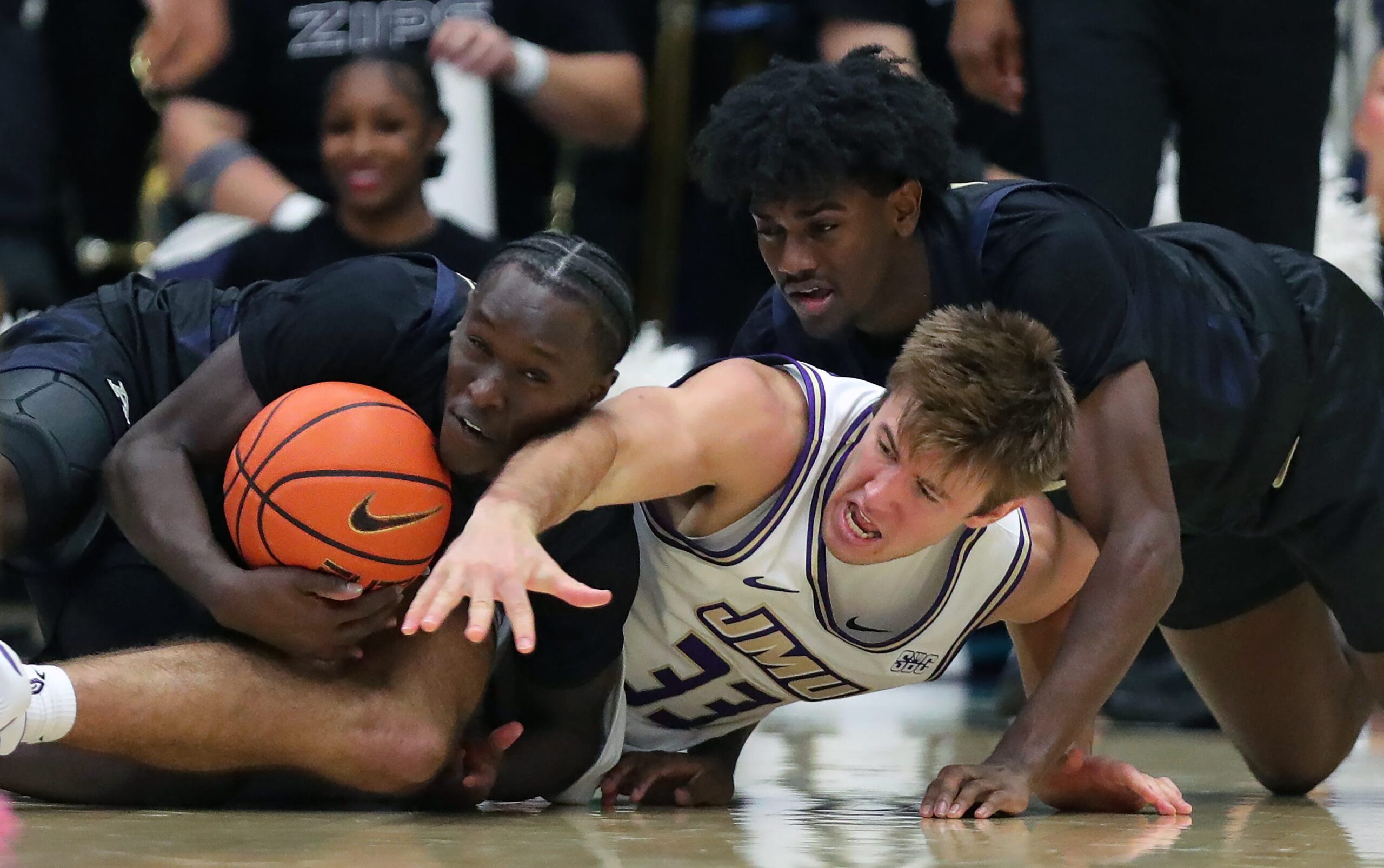 Akron Zips wing Marvin Musiime-Kamali (23) and guard Eric Mahaffey (4) wrestle for possession with James Madison Dukes forward Gabe Newhof (33) during the second half of an NCAA college basketball game at James A. Rhodes Arena, Nov. 3, 2025, in Akron, Ohio