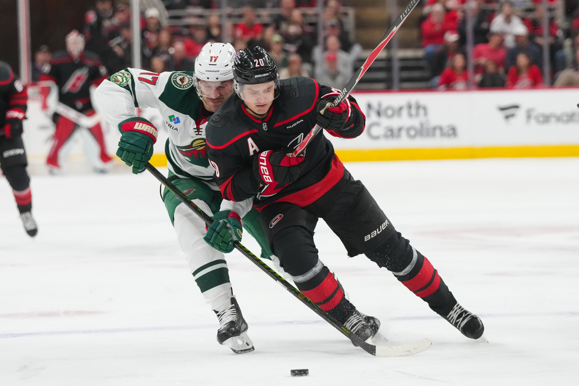 Nov 6, 2025; Raleigh, North Carolina, USA; Carolina Hurricanes center Sebastian Aho (20) skates with the puck against Minnesota Wild left wing Marcus Foligno (17) during the third period at Lenovo Center. Mandatory Credit: James Guillory-Imagn Images