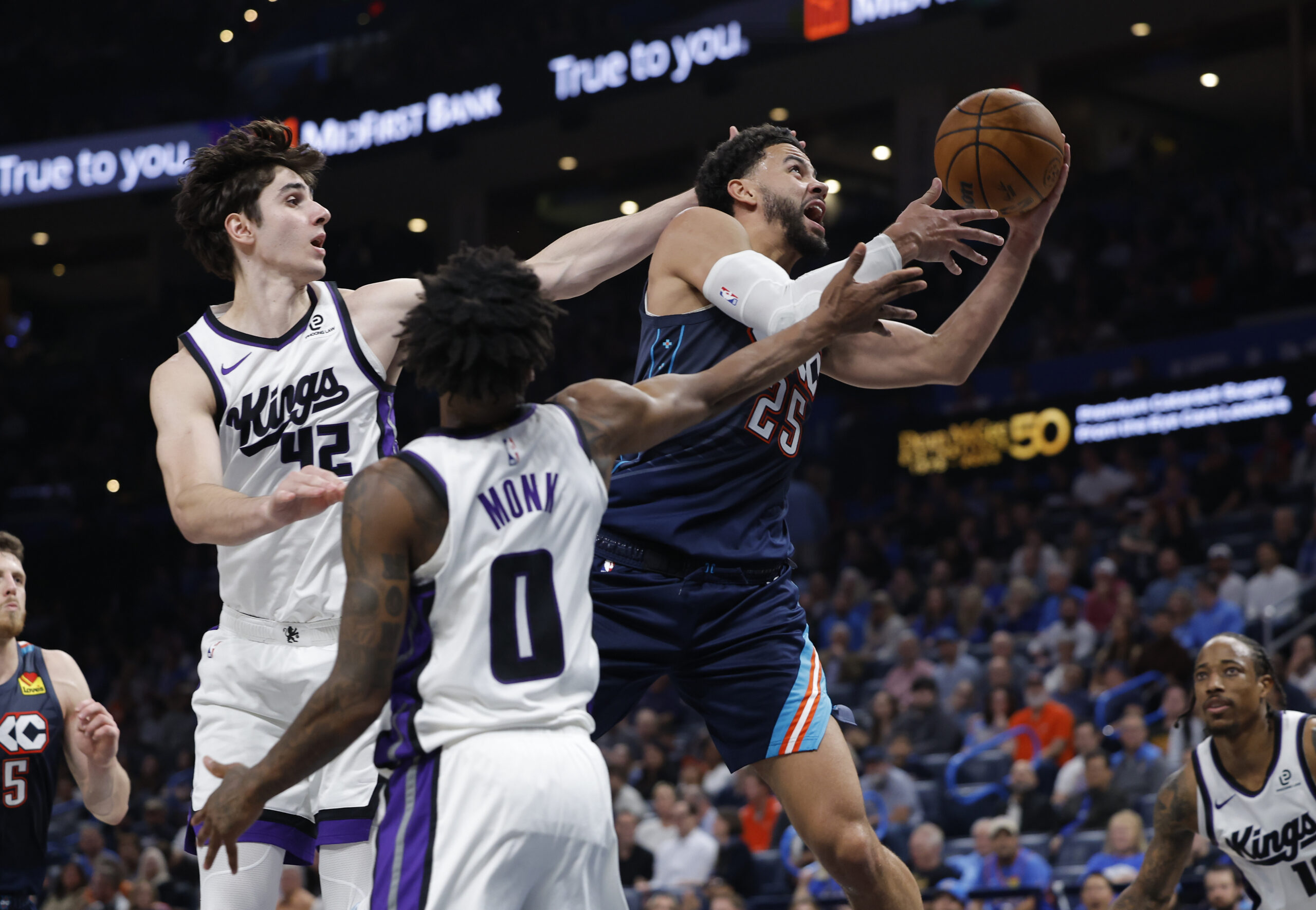 Nov 19, 2025; Oklahoma City, Oklahoma, USA; Oklahoma City Thunder guard Ajay Mitchell (25) goes up for a basket between Sacramento Kings center Maxime Raynaud (42) and guard Malik Monk (0) during the second half at Paycom Center. Mandatory Credit: Alonzo Adams-Imagn Images