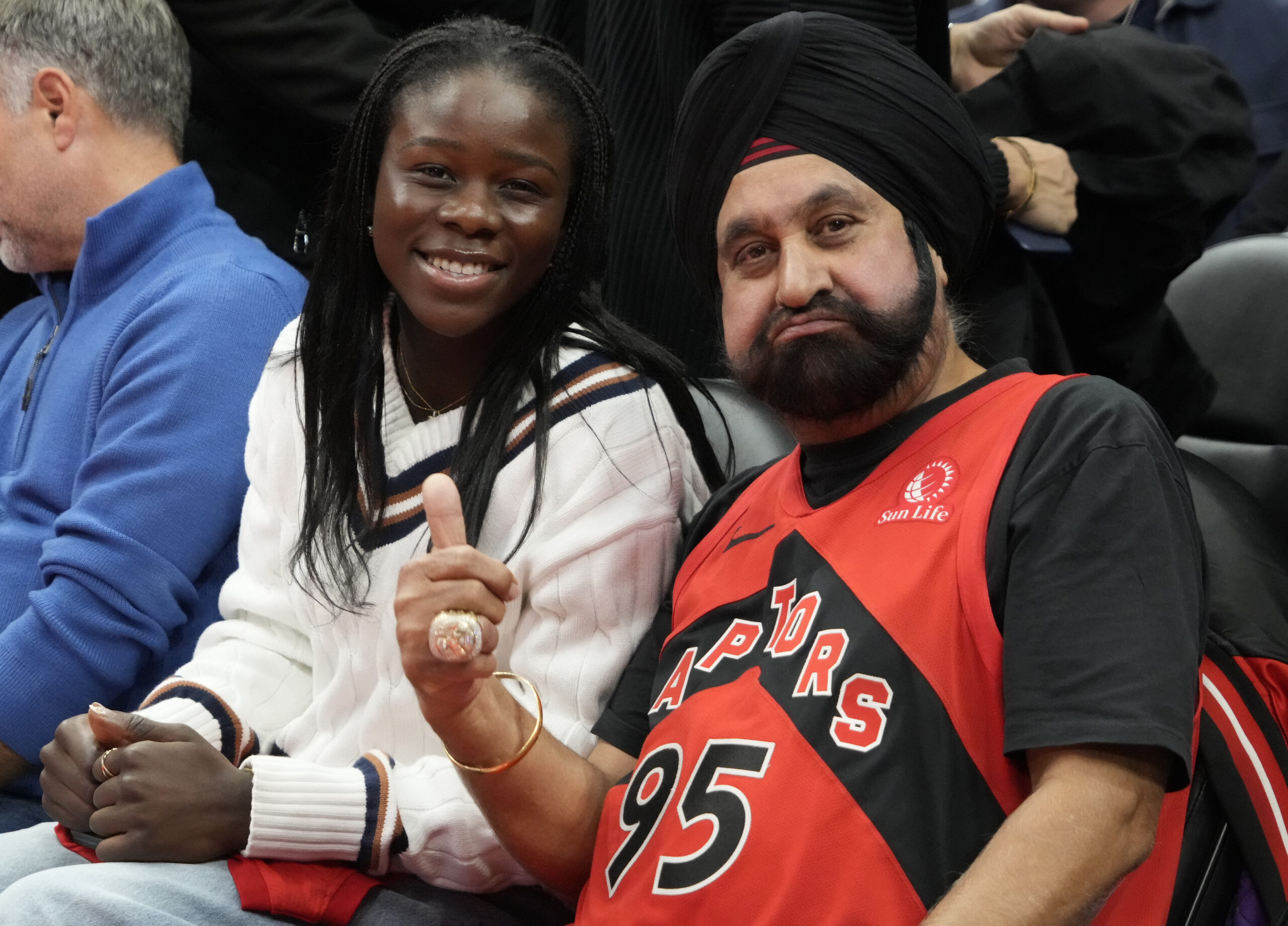 Nov 24, 2025; Toronto, Ontario, CAN; Canadian tennis star Victoria Mboko (left) sits court side with Toronto Raptors superfan Nav Bhatia (right) during a game between the Cleveland Cavaliers and Toronto Raptors during the second half at Scotiabank Arena. Mandatory Credit: John E. Sokolowski-Imagn Images