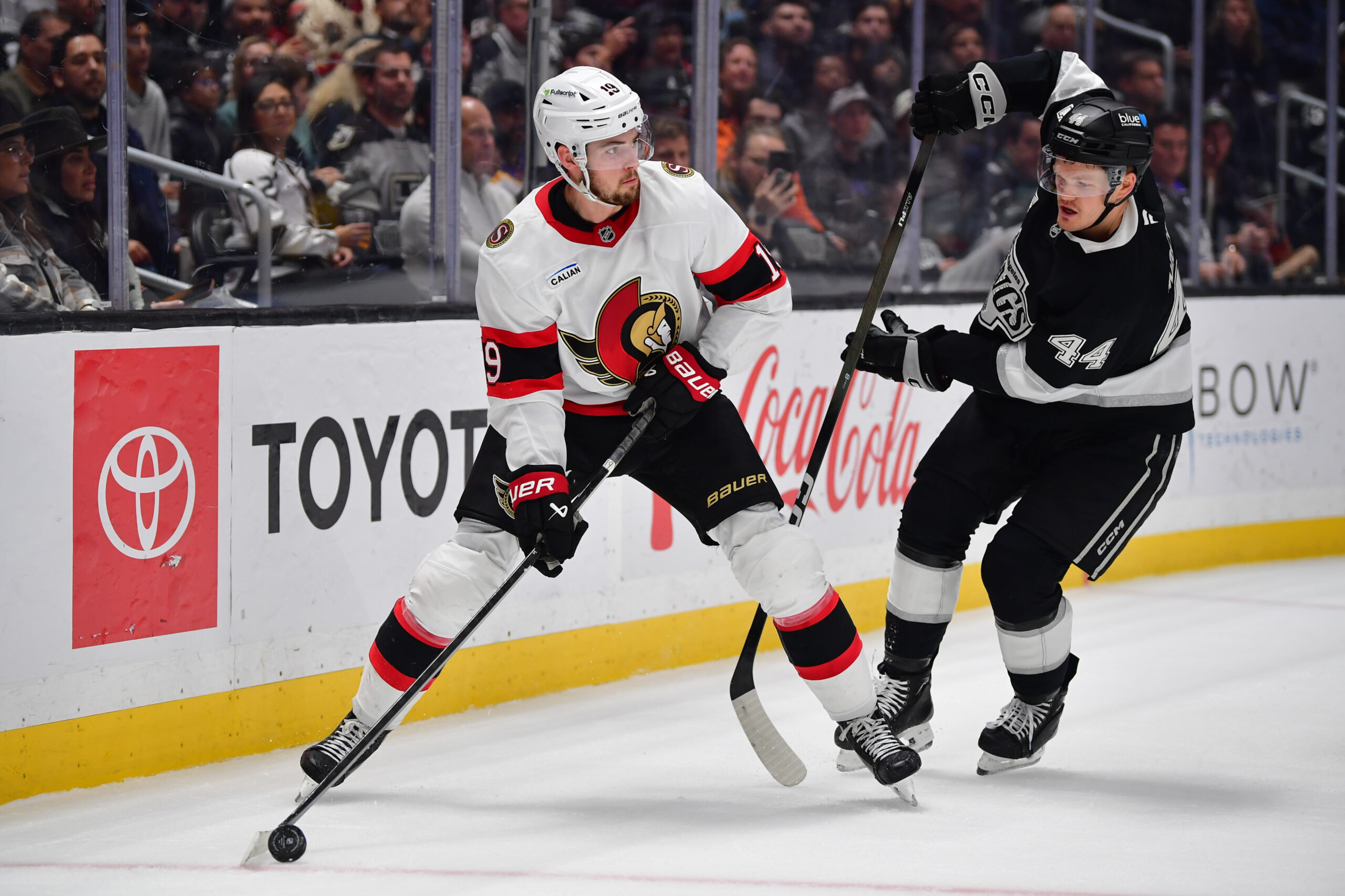Nov 24, 2025; Los Angeles, California, USA; Los Angeles Kings defenseman Mikey Anderson (44) plays for the puck against Ottawa Senators right wing Drake Batherson (19) during the third period at Crypto.com Arena. Mandatory Credit: Gary A. Vasquez-Imagn Images