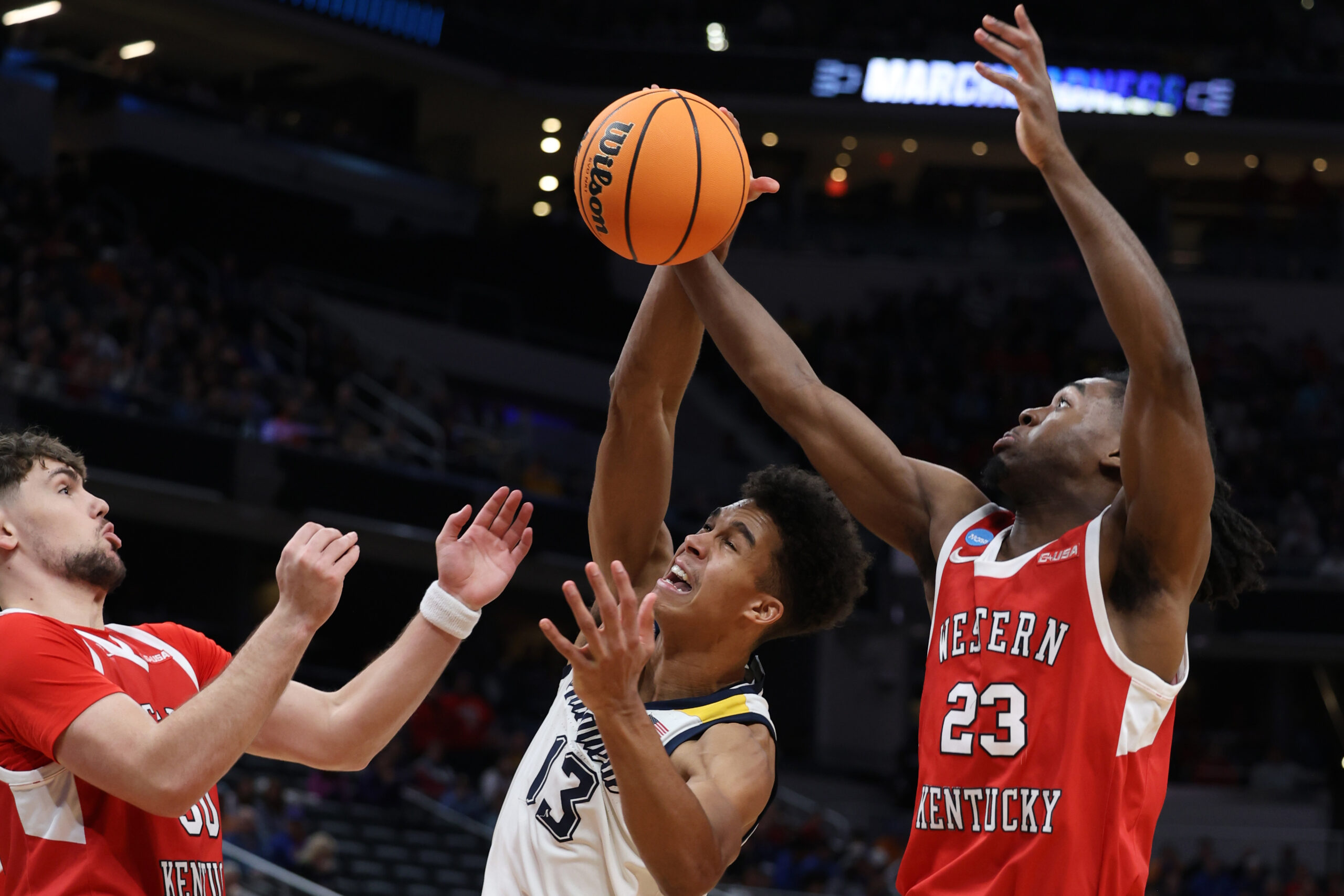 Mar 22, 2024; Indianapolis, IN, USA; Western Kentucky Hilltoppers guard Enoch Kalambay (23) and guard Teagan Moore (30) defend against Marquette Golden Eagles forward Oso Ighodaro (13) in the second half in the first round of the 2024 NCAA Tournament at Gainbridge FieldHouse. Mandatory Credit: Trevor Ruszkowski-Imagn Images