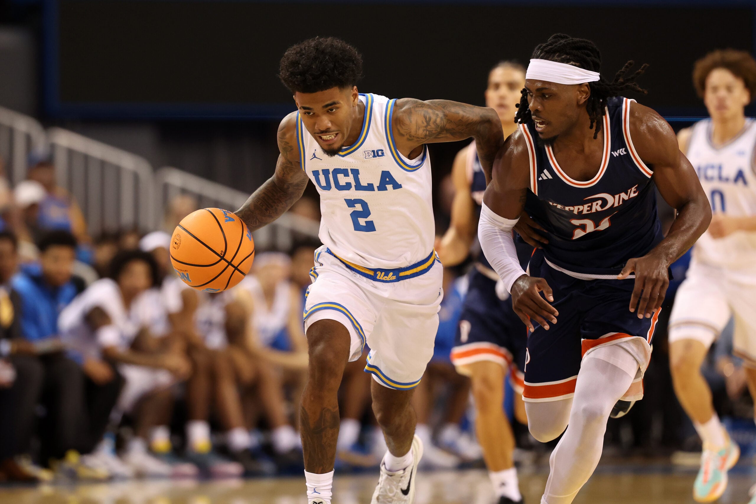 Nov 7, 2025; Los Angeles, California, USA;  UCLA Bruins guard Donovan Dent (2) dribbles the ball against Pepperdine Waves forward Javon Cooley (23) during the first half at Pauley Pavilion presented by Wescom Financial. Mandatory Credit: Kiyoshi Mio-Imagn Images