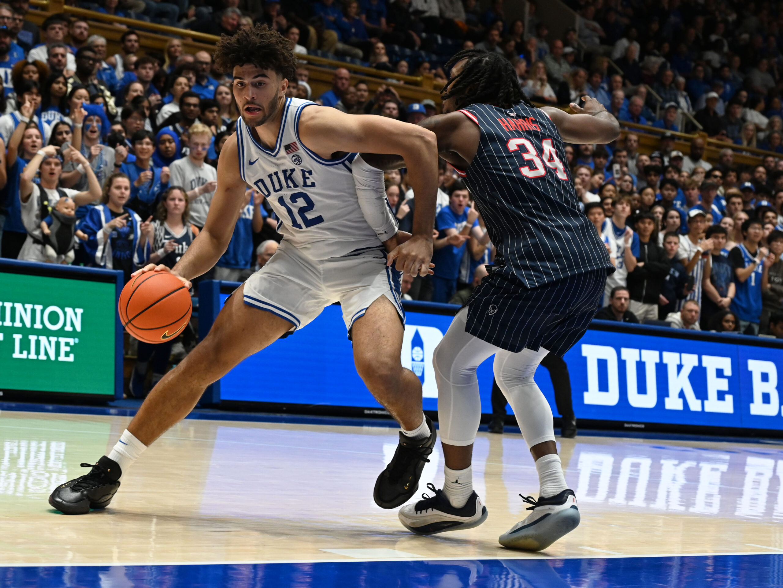 Nov 23, 2025; Durham, North Carolina, USA; Duke Blue Devils forward Cameron Boozer (12) drives to the basket as Howard Bison guard Bryce Harris (34) defends during the second half at Cameron Indoor Stadium. Mandatory Credit: Rob Kinnan-Imagn Images