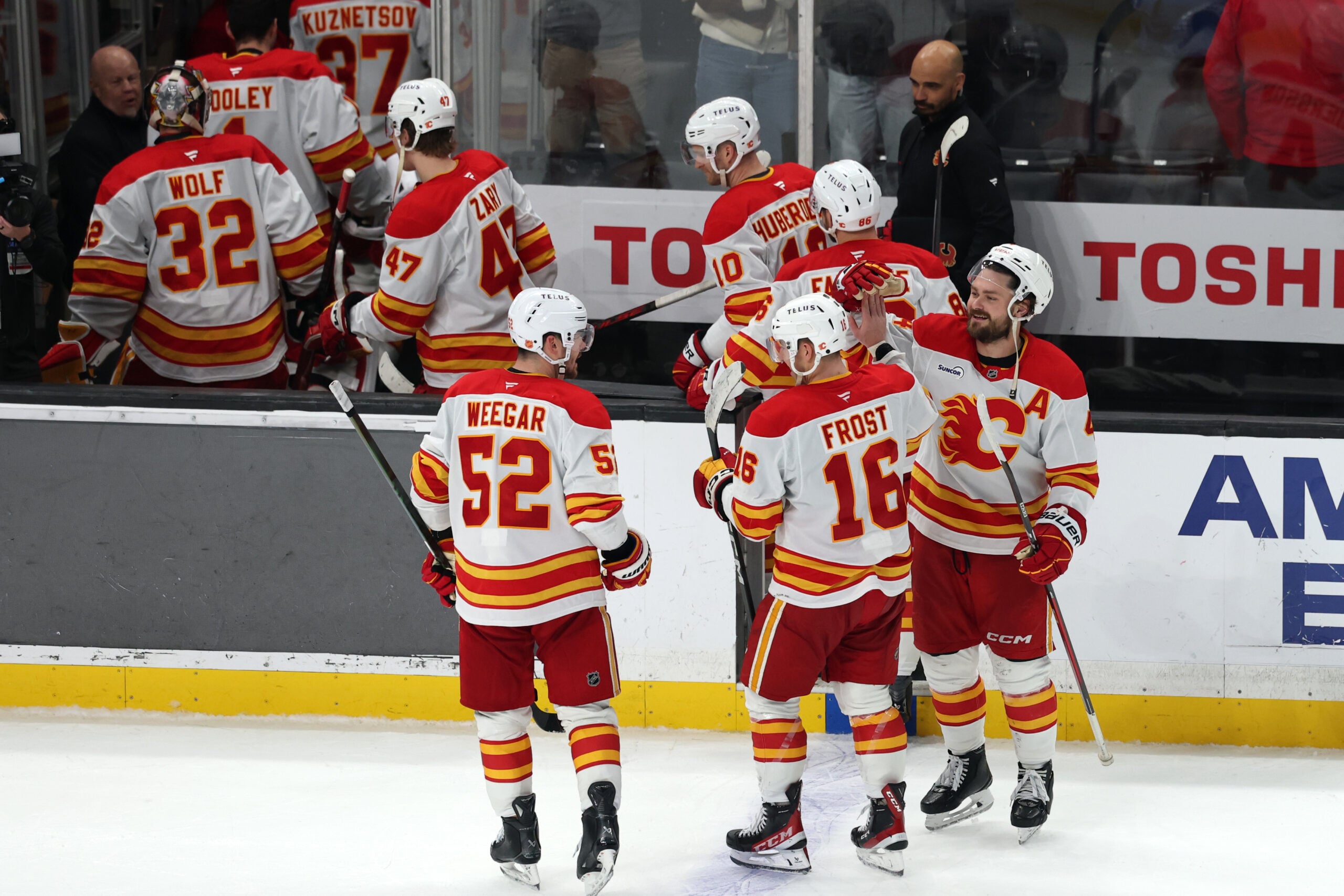 Dec 13, 2025; Los Angeles, California, USA; Calgary Flames center Morgan Frost (16) celebrates with defenseman Mackenzie Weegar (52) and defenseman Rasmus Andersson (right) after defeating the Los Angeles Kings in overtime at Crypto.com Arena. Mandatory Credit: Kiyoshi Mio-Imagn Images