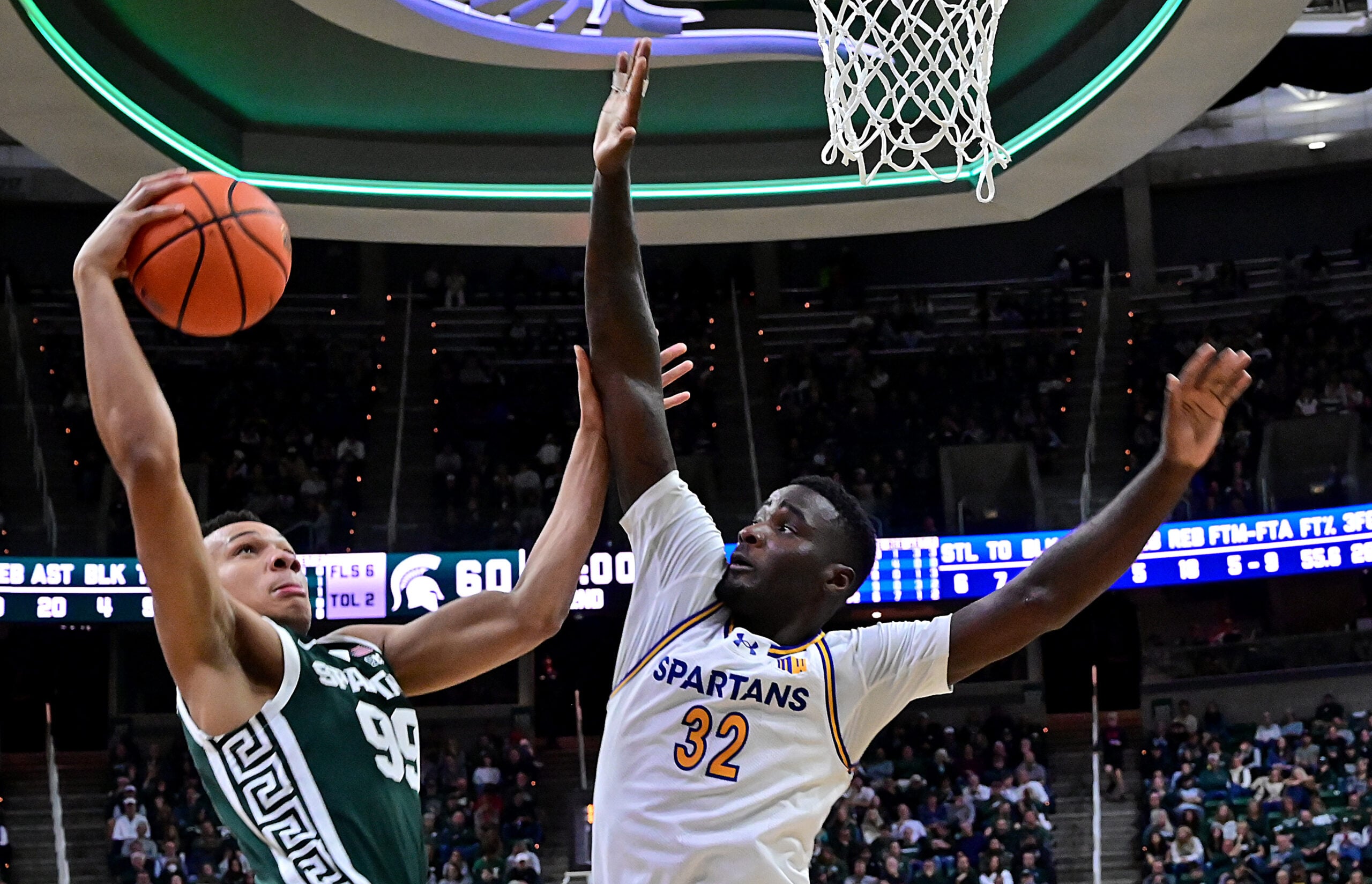 Nov 13, 2025; East Lansing, Michigan, USA;  Michigan State Spartans guard Divine Ugochukwu (99) tries to keep San Jose State Spartans forward Yaphet Moundi (32) away from his shot during the second half at Jack Breslin Student Events Center. Mandatory Credit: Dale Young-Imagn Images
